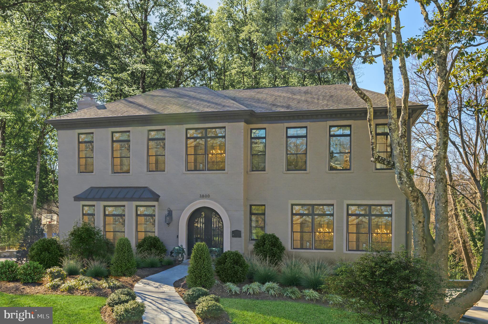 3800 52nd Street NW is an architectural masterpiece blending the pinnacle in design and location. Reimagined from the ground up in 2016, the home is situated on a private third of an acre, amidst verdant rolling hills and distinguished estates. A strong first impression is formed by striking curb appeal courtesy of a painted brick exterior and Pella windows framed with contrasting dark trim. Evoking elements from stylish European villas, the home represents a perfect harmony of international character and contemporary sleekness. Arched glass and wrought iron double doors afford a dramatic entry to the grand foyer, whose soaring ceilings and centerpiece staircase introduce an ethereal floor plan comprising 5,500 finished square feet of luxurious living space. A private office is tucked to one side through double French doors, while formal living and dining rooms opposite the foyer are trimmed with thick crowns, chair rails, and shadow box moldings. Spanning the rear portion of the main level are open-concept informal areas. At the center is the family room, whose accent wall and beamed ceiling feature extensive custom millwork in a nod to the wooded surroundings. Lush views and natural light flood in from a wall of windows overlooking the rear lawn. The kitchen was designed to appease any chef or large-scale entertainer, with extensive inset cabinetry, an oversized center island with integrated seating, a commercial-grade Wolf range top, and a full-size SubZero refrigerator. Its adjacent breakfast nook is relaxed and directly accesses the rear deck. Upstairs, the primary suite’s barreled ceiling is yet another testament to the quality of construction, while a private balcony affords blissful views. In the marble-clad, spa-inspired bath, all of the expected accouterments prevail, not limited to separate vanities, an artistic freestanding soaking tub with wooded views, and a walk-in glass shower with multiple jets. An ample closet space replete with custom built-ins completes the picture. Three additional bedrooms, each generous in scale and boasting both ensuite baths as well as walk-in closets, complete the upper level. A large recreation room with stacked stone fireplace framed by built-ins anchors the daylight lower level. The similarly extensive wet bar further enables entertaining, while a full bedroom suite, laundry facilities, powder room, and access to the oversized two-car garage greatly enhance the home’s overall livability. Out back, extensive hardscaping surrounds the large patio which descends down into a flat, grassy area. The elevated lot, wooded surroundings, and total privacy are true distinguishing factors and rare luxuries in the city. Feeling a world away from downtown with its natural setting and extensive premium amenities, yet always remaining within easy reach, 3800 52nd Street NW is an unequivocally fine representation of Washington’s best.