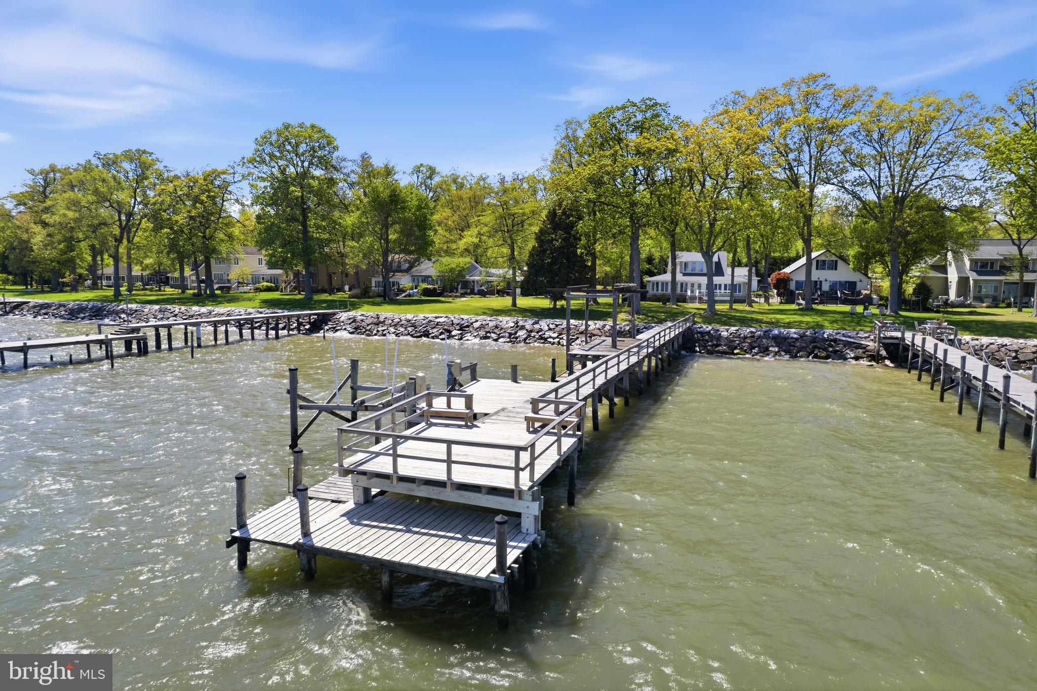 Experience stunning Chesapeake Bay views from this beautiful waterfront Cape Cod. One of the longest and widest private docks in Holland Point sets the tone, complete with a boat lift, multiple sun decks, fishing platforms, and a 5' MLW. Inside, the great room is lined with wall-to-wall windows, flooding the space with natural light and unparalleled water views. The kitchen carries the theme with panoramic bay views, granite countertops, white cabinetry, stainless steel appliances, and a breakfast bar perfect for casual dining. This thoughtfully designed home offers a full master suite on each floor, each featuring a walk-in closet, a large bathroom, and a laundry room on both floors. The first floor also includes an additional bedroom with its own bathroom, a fourth full bathroom, and a comfortable sitting room. Brand-new premium carpet flows throughout both floors, complemented by original hardwood in the common areas. Meticulously maintained, the home features a recently replaced roof, HVAC system, plumbing upgrades, gutters, and drainage system. The brand-new rear deck gives you the perfect place to sit and soak up the view. Herrington Harbor is just a short distance away, with fine dining options in both directions.