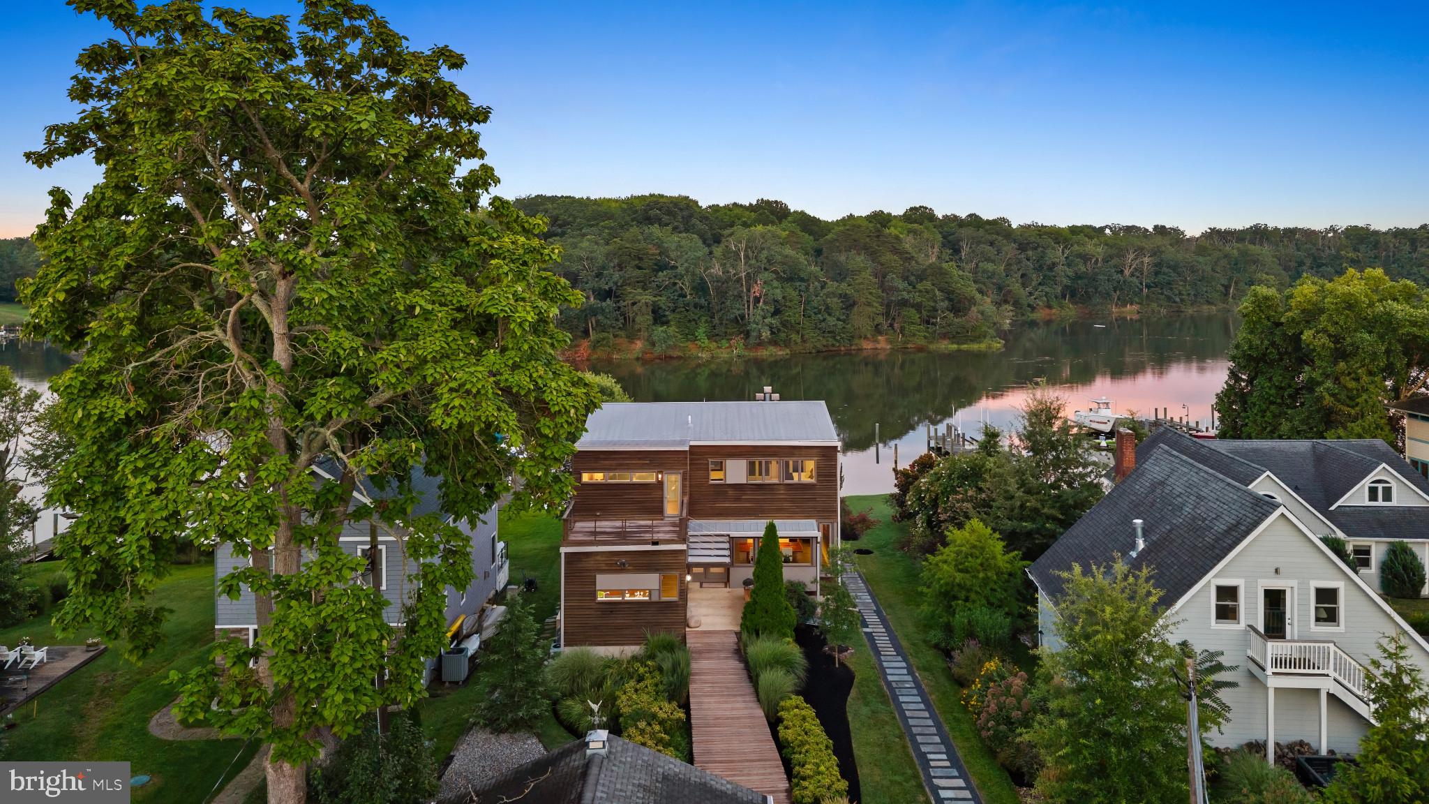 Situated on .63 acres of private waterfront, this award-winning contemporary home offers commanding views of Harness Creek and the protected woodlands of Quiet Waters Park across the water. Designed by renowned New York-based architects Robert Luntz and Joseph Tanney of Resolution: 4 Architecture, and expertly constructed by John DelSesto, this 2006 Metropolitan Modern Home of the Year exemplifies custom modular design at its finest. A radiant-heated IPE wood walkway leads you to the striking front entrance. Inside, the main level boasts a seamless, open-concept layout where the kitchen, dining room, and fire-placed living room flow effortlessly together. Expansive water views pour in through floor-to-ceiling windows and two sets of sliding glass doors that lead to a spacious main-level deck. The Bulthaup kitchen is a showpiece, featuring a Kohler sink, custom poured concrete island with seating for four, stainless steel countertops, and high-end appliances from Miele, Asko, Sub-Zero, and Wolf.  The kitchen sink offers a perfect vantage point to enjoy the water while you cook. Down the hall you'll find a butler’s pantry with wet bar, powder room, and a private side entrance, ideal for entertaining or to be used as a mudroom space. The ground level offers an exceptional blend of comfort and functionality, featuring a private suite bedroom, an office and a sitting area. Bedroom highlights include a gas fireplace, dual walk-in closets, and a spa-like ensuite bath with a double vanity, walk-in shower with teak flooring, and a private water closet. Enjoy seamless indoor-outdoor living with direct access to the patio with outdoor shower and easy access to the water to complete the space. The top level of the home is designed for elevated living and effortless entertaining. It features a bright entertainment room, a full bathroom with a soaking tub offering stunning private water views, and a bedroom with vaulted ceilings that enhance the sense of space and light. This floor also boasts two distinct outdoor spaces: a rear deck facing Harness Creek with a beautiful outdoor wood-burning fireplace, perfect for entertaining guests or relaxing by the fire as the sun sets over the water, and a front-facing balcony that offers tranquil treetop views and a peaceful escape for quiet mornings and stunning sunsets. A separate detached structure offers the ideal studio or creative workspace. This versatile building includes a welcoming front room perfect for use as an office, art studio, or fitness room. The building also features a full bathroom and a large open area with limitless opportunities. The outdoor space is as thoughtfully designed as the interior, with multiple decks that maximize the waterfront views and create seamless indoor-outdoor living. The property includes a private dock with deep water (6–8 feet MLW), water and electric service, two boat lifts, sailboat slip, a floating dock ideal for kayaks/paddle boards and access for a rowing shell—making it a true waterfront enthusiast’s dream. With its modern design pedigree, refined materials, and unbeatable location just minutes from downtown Annapolis, this architecturally significant home offers a rare opportunity to own a one-of-a-kind waterfront retreat in one of the region’s most sought-after settings.