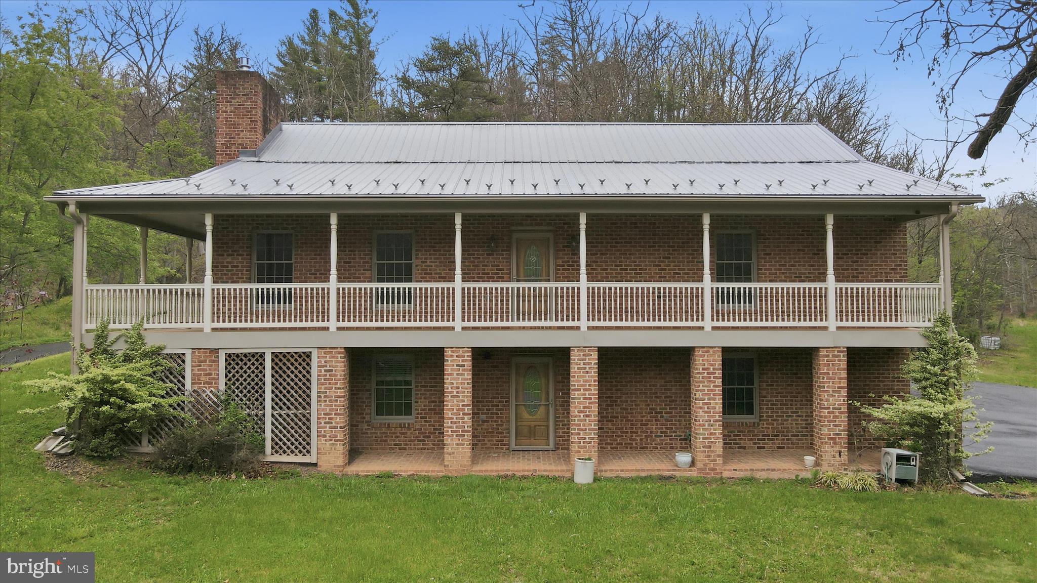 The main house is a two-story custom built brick home with a metal roof and two story wrap-around porch.  Main level features mostly hardwood floors, an eat-in kitchen with island, dining area, laundry area off kitchen, living room with brick fireplace, two bedrooms with walk-in closets, full bath, primary bedroom with a full bathroom, walk-in closet and walk out to the back porch. The basement has a large family/rec room with a fireplace, a utility room, a full bathroom and an attached oversized 2-car garage. The home has central air, an alarm system, water softener and backup generator. The property also offers a rippling stream, wooded acreage, a root cellar, pole barn with 200 amp service, another storage building and a historic log home in need of repair. The log home has no electric or water and was known as a stagecoach stop in the 1800’s.   All this in a private rural setting but with convenient access to major roadways. Don't miss out! 1 Year Home Warranty Included.