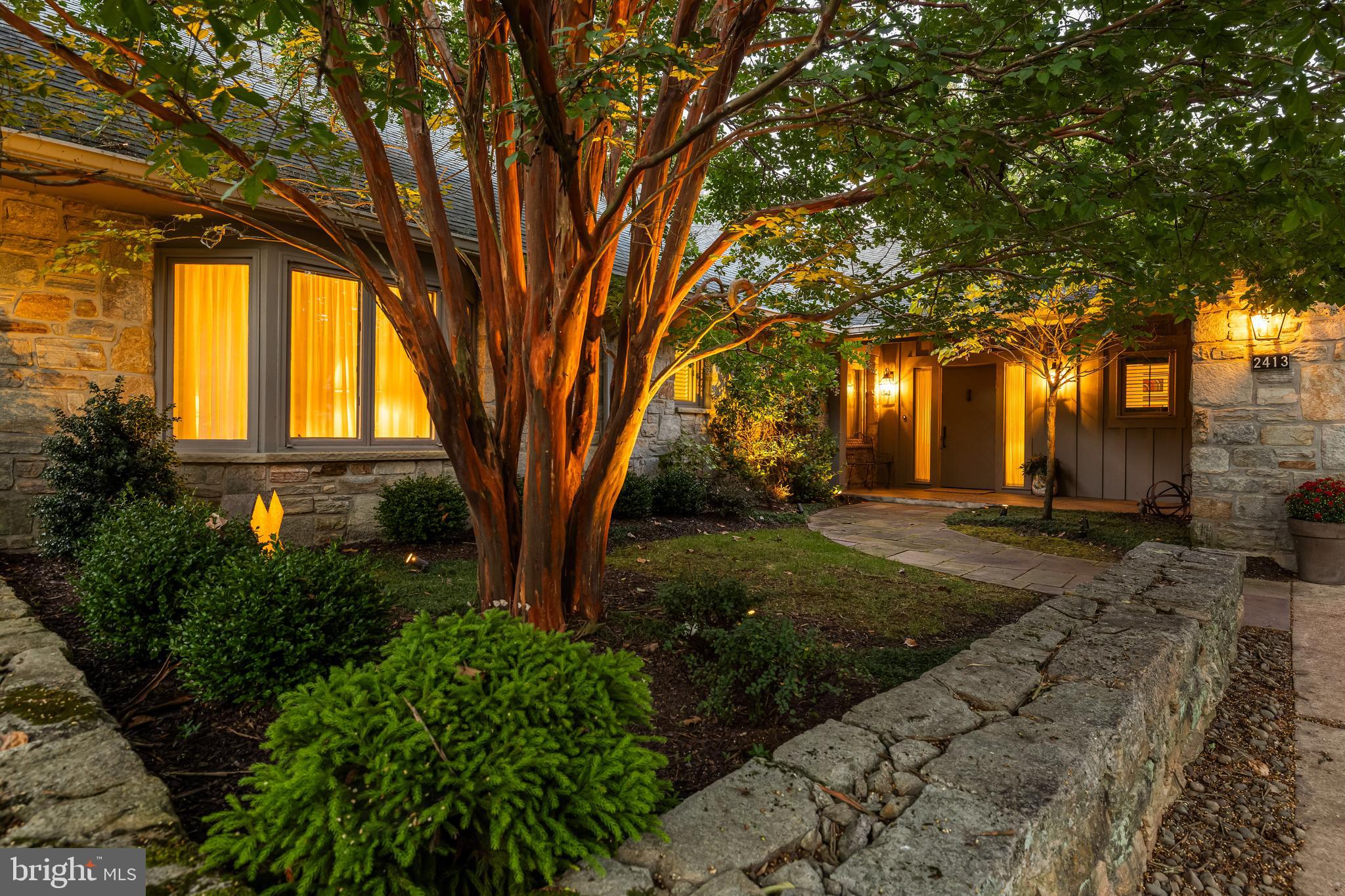 A stone stone-walled entry garden with a stone walkway leads to the covered porch of this luxury home, seamlessly expanded & thoroughly updated. Beautifully sited on one of the finest lots in the gated Rockland community, backing to green space. Easy one- floor luxury living with the added dimension of a walk-out finished Lower Level that includes a Rec Room with fireplace and wet bar, a sunny Studio/Crafts Room and Bedroom 3/Guest Room and full Bath. A warm wood-paneled Foyer leads to the Living Room through a post-and-beam portal and to the Family Room. This exceptional residence at 2413 Still Forest Road offers 3 bedrooms, 3/1 baths, and over 5,000 square feet of richly appointed living space, blending architectural charm with thoughtful updates. Located just minutes from Green Spring Station and major commuter routes, it’s a rare offering in one of Baltimore County’s most desirable neighborhoods. The main level unfolds with a balance of formal and informal spaces. The expansive Living Room is a focal point, anchored by a striking stone fireplace with gas insert and flanked by dual access points to the sunroom. Wide-plank hardwood floors and a beamed ceiling add to the room’s character, while triple windows and a door to the elevated deck connect the interior to the serene outdoors. Flowing directly from the Living Room, the Dining Room offers generous proportions and rich finishes, including another beamed ceiling, wide-plank floors, and built-in ceiling speakers, creating an ideal setting for hosting dinner parties or holiday gatherings. The Kitchen is truly extraordinary, both in scale and craftsmanship. Custom white Shaker cabinetry surrounds a substantial contrasting island, all topped with granite and complemented by a marble backsplash. Gourmet appliances are seamlessly integrated, and a matching wet bar includes a second dishwasher, wine coolers, and an icemaker. A built-in desk, dual pantry closets, and walls of built-in shelving add exceptional function, while a skylight and breakfast area with banquette seating provide a warm, inviting spot to gather. The Sunroom features vaulted wood-paneled ceiling, & 3 sets of floor-length windows, offering a peaceful transition between indoor comfort and outdoor beauty. A warm, comfortable Family Room offers a wall of custom built-in cabinetry and glass door to a stone Patio. Privately tucked away on the main level, the bedroom wing includes a luxurious Primary Suite with a bay window alcove, custom built-ins, and two fully outfitted dressing rooms. The marble-clad Primary Bath offers dual vanities, a Bain Ultra soaking tub, and a spa-style shower with multiple sprays and a built-in bench. Bedroom 2 also enjoys its own bay window seating area and custom fitted closets, with easy access to a beautifully finished full bath. A stylish Powder Room near the Foyer adds additional convenience for guests. The finished lower level provides additional living space with its expansive Recreation Room, featuring a second stone fireplace, custom bar, and built-in shelving. A Studio space with three sliding glass doors and a wall of cabinetry offers a flexible zone for creative work or hobbies. The third Bedroom on this level is generous and private, with two walk-in closets, one cedar-lined, and access to a full bath with marble finishes and a walk-in shower. Additional built-ins, a workshop, and large closets complete this highly functional space. Outside, the property is a showcase of thoughtful landscaping and private outdoor living. The elevated deck, accessible from both the Kitchen and Living Room, includes a retractable awning and gas grill hookup, while stone patios and garden walkways connect seamlessly to the natural surroundings. The backyard flows gently toward a wooded hillside, offering privacy and a sense of retreat. New 2026 roof,  Tamko Rustic Black with transferable 10-year warranty for labor.