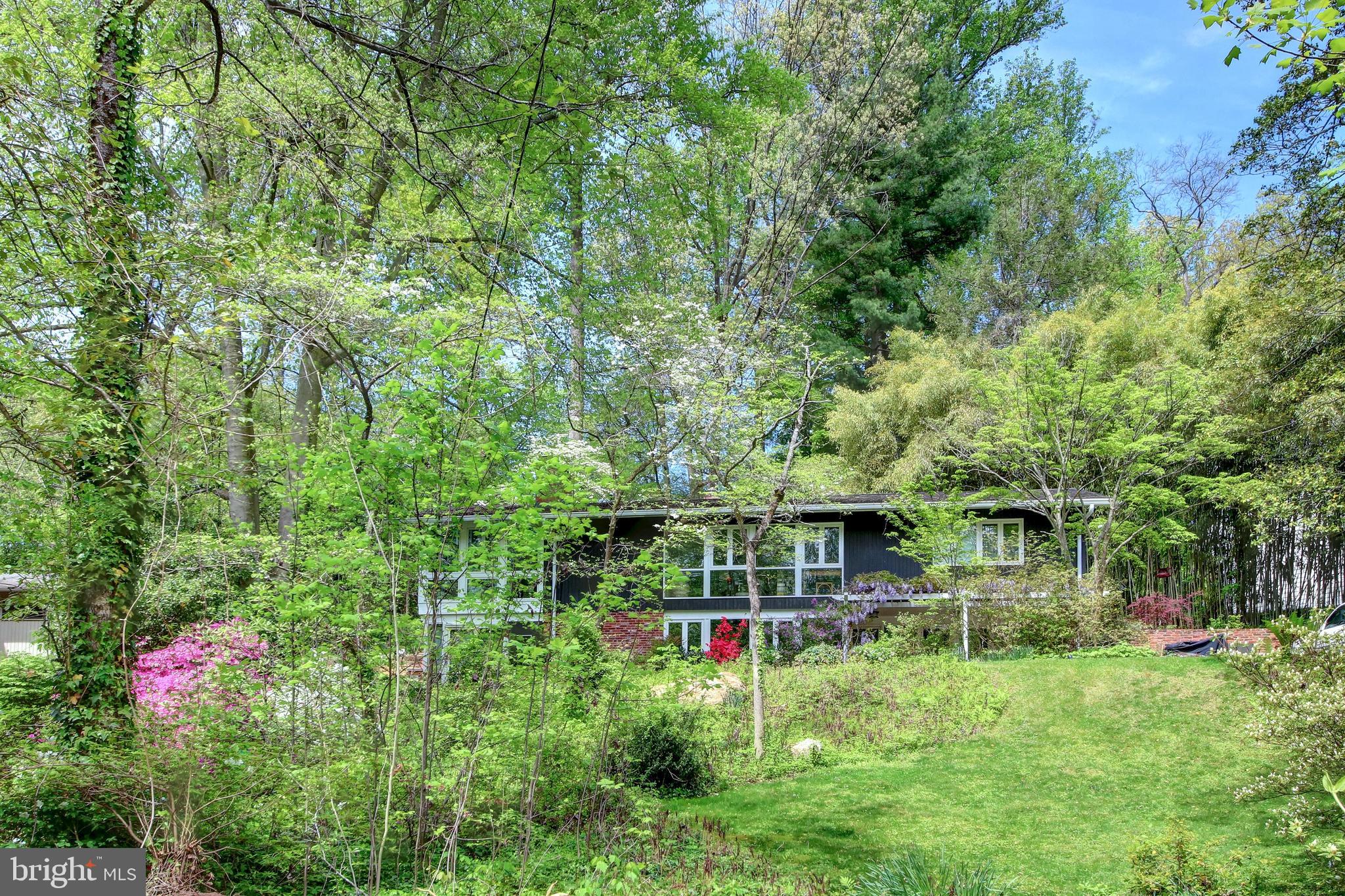 Incredible, new price for this mid-century house, prominently set amongst mature plants and trees with expansive glass windows and lush, green views all around.  The interior is spacious and comfortable and offers an open floor plan that works well for family gatherings, relaxed get-togethers with friends, or larger scale events.  In addition, the flow from the interior space to the exterior space is seamless, making it perfect for all styles of entertaining.  Multiple glass doors open to the multiple outdoor, seating areas, creating a natural extension of the living space.  Whether in or out, this is the ideal spot to live, enjoy and create a lifetime of memories.  The main entrance has a quaint, outside sitting area with a wisteria trellis above.  Upon entering, there is an open foyer, a large family room with fireplace, and a true, glass-enclosed studio – ideal for artists, yogis, the fitness conscious, or someone in need of a home office that also has easy access to the garden beyond.  There are two bedrooms and a full bath also on this level.  The upper level is a surprise with a large living room and dining area that is open and airy with multiple windows that provide a connection to the outdoors.  Just off the living and dining rooms is a glass-enclosed sunroom, adding an extra layer of versatility and charm.  This might easily become a favorite spot for casual entertaining, curling up with a good book or having a quiet moment to yourself.  It also makes a great home office with so much natural light in a place that truly feels private and tranquil.  The kitchen is modern and spacious with ample countertop and storage space.  It will work well for any level of chef and has an island for a more casual gathering as well as a charming breakfast/dining area surrounded by natural light.  The primary bedroom with en-suite bath and an additional bedroom with hall bath complete this level.  Overall, 7108 Broxburn Drive embodies the mid-century modern ethos of simplicity and functionality while also providing a gracious, inviting and comfortable place to call home.