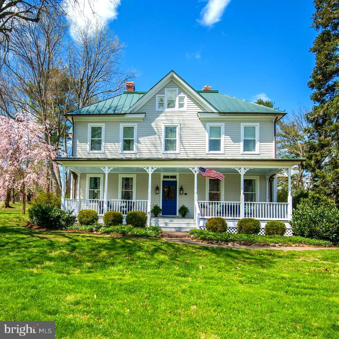 Rural Hill is one of those homes you drive by and never forget. Perched on a gentle hill with its welcoming front porch and the ever-present American flag waving in the breeze, it catches the eye of all who pass. A familiar landmark in the quaint village of Paeonian Springs, Virginia, its charm is undeniable.

Built in 1904, the home has been beautifully restored and reimagined as a Modern-Day Farmhouse, set on nearly four acres with sweeping pastoral and mountain views. Step inside, and you’ll immediately feel the warmth and character that only a historic home can offer. The Family Room, just off the kitchen, features a custom wood bar handcrafted by Shenandoah Furniture. Thoughtful touches throughout pay homage to its past—the attic bathroom door, repurposed from the original barn wood, and the barn’s party room shutters, which once adorned the house itself.

Spacious rooms with ten-foot ceilings, original wood floors, built-in bookshelves, and pocket doors reflect the craftsmanship of another era. While its historic beauty has been lovingly preserved, the home has been thoughtfully updated with new doors and windows, modern systems, and carefully selected light fixtures and surfaces that blend seamlessly with its classic style. The kitchen, a perfect balance of old and new, retains its 1904 soul while offering top-tier modern conveniences. Rich wood tones, timeless details, and a welcoming atmosphere make it a place where people naturally gather, whether to cook, share meals, or simply linger.

The breakfast room, with its double French doors, opens to a terrace-style outdoor living space—an intimate retreat with flagstone benches, a fire pit, and a stone waterfall tucked beside the pergola. The main floor den, awash in natural light, is ideal for remote work with Comcast high-speed internet, while the front study offers a peaceful spot for reading or reflection. The formal dining room, uniquely connected to the front porch, is an unforgettable setting for shared meals and celebrations.

Upstairs, the owner’s suite is bathed in light, with windows framing views of the changing seasons. The modern bath features a walk-in spa shower and a spacious double vanity topped in Carrera marble. Three additional bedrooms share a stylish, updated bath, while the finished attic serves as a cozy retreat, complete with a fifth bedroom, game area with window nook and a full bath. Every inch of the home radiates a sense of peace and comfort.

Outside, mature gardens, specimen trees, and thoughtful hardscaping frame breathtaking views of the Blue Ridge Mountains. The Party Barn, located in the 2- car garage, with its soaring ceilings and spectacular vistas, is an ideal gathering place for any occasion. A fenced paddock provides space for horses or future four-legged friends.

One of the home’s most functional and delightful spaces is the mudroom—a room in its own right. Designed with daily life in mind, it offers built-ins, a full-sized washer and dryer, a sink, and designated spots for dog beds, coats, and sports gear. At its center, space for a large farm table invites everything from arts and crafts to wrapping presents or simply staying organized. A door leads directly to the terrace, and a conveniently located half bath is just steps away.

The enchanting pea gravel driveway, reminiscent of an English country estate, adds to the home’s storybook charm. Though it feels like a world apart, this home is minutes from historic Leesburg, with easy access to restaurants, coffee shops, art galleries, and boutiques. The Washington & Old Dominion Trail is just down the street, and the Dulles Greenway, five minutes away, makes travel effortless—whether heading to D.C., IAD, or nearby Reston. Even the Leesburg Executive Airport is just ten minutes away.

This is more than a house—it’s a place where history, beauty, and modern comfort come together in a way that simply feels like home.