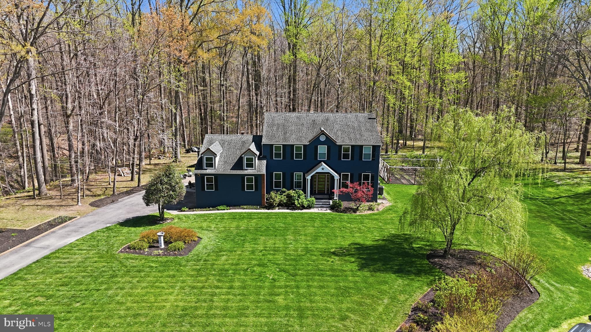 Welcome to 3205 Ivy Way — a beautifully reimagined colonial set on a private, wooded lot in the heart of Harwood, Maryland. From the moment you arrive, the home commands attention: a striking navy-blue exterior with warm cedar accents, a custom address fountain at the entry, and lush, manicured grounds framed by mature trees. The sweeping driveway leads to an attached 2-car garage complete with a built-in drop zone — a practical and polished place to land after a long day.
Step through the custom double wood-and-glass front door and you're immediately greeted by a welcoming foyer with board-and-batten wall detailing, brand new luxury vinyl plank flooring, and a dramatic cascading linear chandelier that draws the eye upward. The main level has been thoughtfully designed for the way people actually live — offering multiple distinct spaces without ever feeling disconnected. A sun-filled den with French doors off the entry provides the perfect private retreat for working from home, with views of the front yard and easy access to the foyer. The formal living room is a refined, light-filled space ideal for entertaining, while the separate formal dining room impresses with wainscoting, crown molding, tile floors, and a bold statement light fixture. The heart of the home is the open-concept kitchen and family room — the kitchen stuns with rich espresso cabinetry, a quartz waterfall island, stone tile backsplash, gas range, and stainless appliances, while the adjacent breakfast area bathed in natural light flows seamlessly into the family room, where a wood-burning fireplace with painted surround anchors the space. French doors off the family room open directly to the back deck, making indoor-outdoor living effortless. Rounding out the main level is a jaw-dropping powder room — a true design moment featuring bold geometric gold-veined wallpaper, a statement green vanity with brass hardware, and an arched mirror with sconce lighting on each side.
Upstairs, the primary suite is a true sanctuary, featuring a stunning luxury American walnut slat wood wall panel accent, a ceiling fan, and a spa-level bath that stops you in your tracks — dual vanities with herringbone-front cabinetry, quartz counters, matte black fixtures, an oversized walk-in rainfall shower with designer mosaic tile accents, built-in niches, and a freestanding soaking tub framed by a wall of windows overlooking the treetops. Three additional bedrooms — each with its own personality and generous closet space — and a well-appointed shared bath complete the upper level. The spacious unfinished basement offers a blank canvas brimming with potential — whether you envision a home theater, gym, game room, or additional living space, the footprint is ready for your vision, and a wood stove already in place adds warmth and character to whatever comes next. Outside, the backyard is an entertainer's dream unlike anything in the neighborhood: a wooden deck with string lights leads to a stunning custom pergola set on its own dedicated wood platform, fully outfitted with a louvered aluminum roof for year-round use, flowing privacy curtains, and a full lounge seating area — all surrounded by a lush, private tree line that makes it feel like your own secluded retreat. For those with a green thumb, a large custom-built garden enclosure with raised beds and electric fencing offers the ultimate setup for growing your own fruits, vegetables, and herbs in true farm-to-table fashion. Solar panels add modern efficiency to the package. Located just 14 miles from Annapolis, 30 miles from Washington D.C., and within easy reach of the Chesapeake Bay, 3205 Ivy Way is southern Anne Arundel County living at its absolute finest.