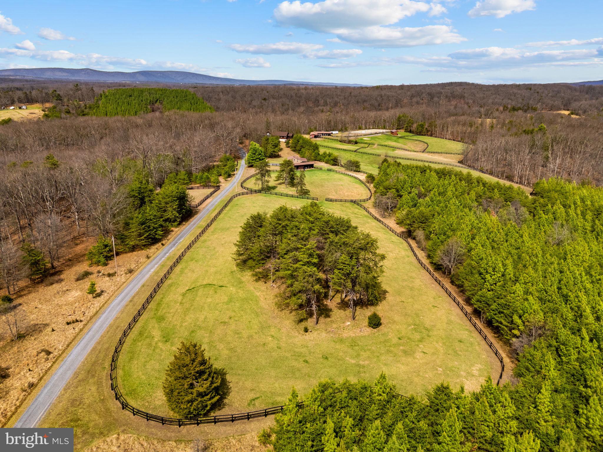 Set on 65 picturesque acres just outside of Winchester, 632 Dry Creek Lane offers a rare blend of refined living and exceptional land, an ideal private retreat within easy reach of Washington, DC. Designed for comfortable single-level living, the 4-bedroom, 4-bath home offers approximately 3,367 finished square feet filled with natural light and sweeping countryside views.
A dramatic vaulted great room with stone hearth and gas fireplace anchors the home, while the spacious kitchen features quality cabinetry, an oversized island, and a layout that opens to the main living areas. The main-level primary suite provides a private retreat with screened porch, dual walk-in closets, and a redesigned bath.
Additional highlights include two main-level bedrooms, a newly enclosed loft bedroom with balcony, and a full walkout basement with full bath for future expansion. A peaceful creek winds through the property, complemented by established riding and walking trails.
Equestrian amenities include two barns, a 100’x200’ lighted arena, 10 fenced pastures, and run-in sheds. A custom recreation barn offers additional finished space with indoor and outdoor entertaining areas, completing this peaceful, turnkey escape with exceptional versatility.