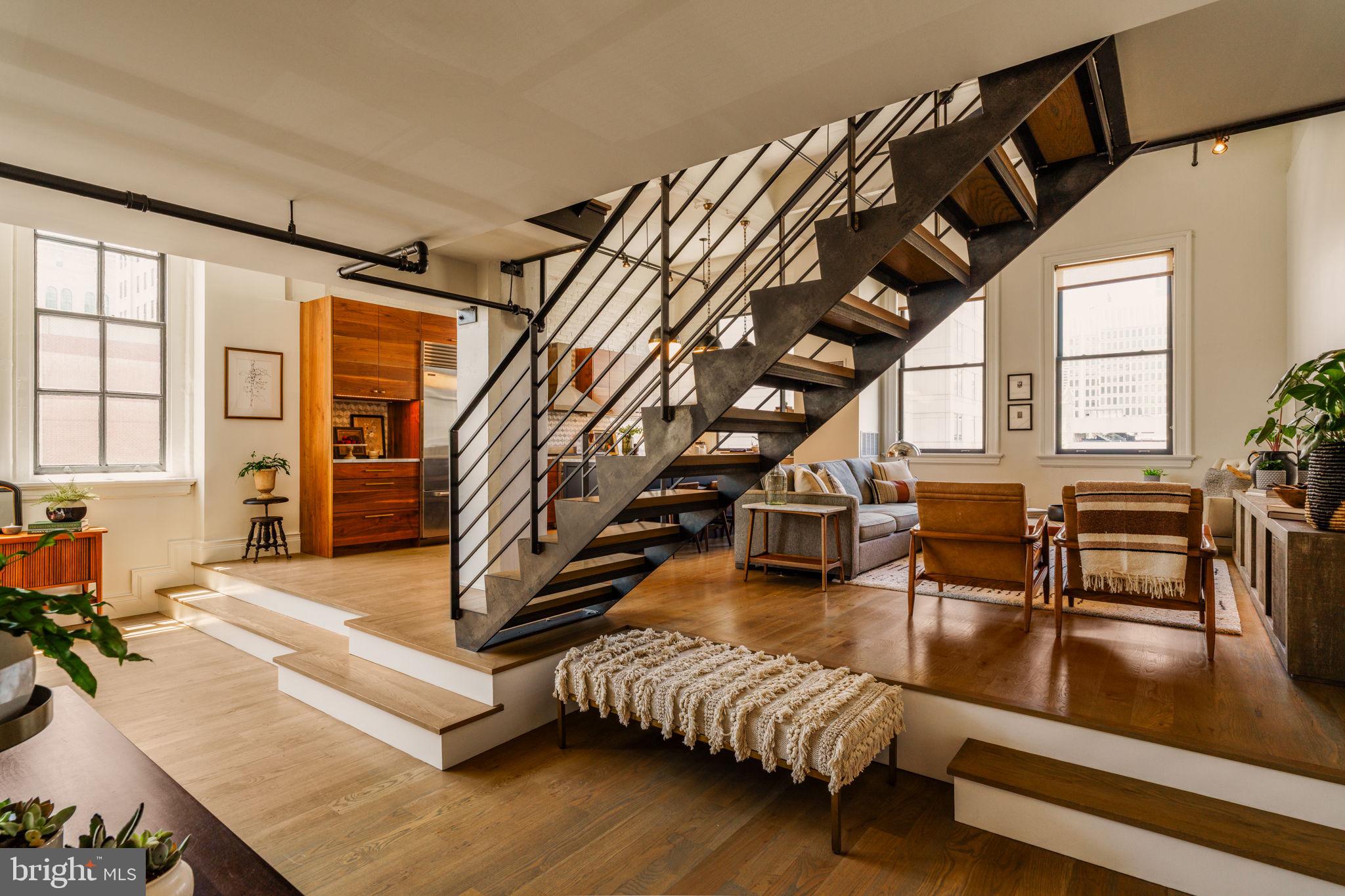 Residence 8E at The Arch Street Exchange, an irreplaceable penthouse that represents a singular expression of craftsmanship, design, and architectural character. Featured in Domino Magazine and masterfully conceived by acclaimed Philadelphia design studio Rohe Creative, this highly customized home presents a rare opportunity to own a truly collectible piece of residential design.

Offering two spacious bedrooms, two full bathrooms, and approximately 2100 square feet across three levels, the residence is crowned by an exceptional private rooftop terrace spanning approximately 500 Sq Ft, an extraordinary extension of the home’s living space.

From the moment you enter, the home’s bespoke character is unmistakable. Every surface, material, and architectural detail has been thoughtfully curated and meticulously executed, resulting in a residence of remarkable warmth, depth, and refinement. Continuous-grain millwork, custom steel-and-glass architectural elements, reclaimed wood accents, unlacquered brass fixtures, and layered designer finishes create an atmosphere that is both sophisticated and deeply inviting. The thoughtfully designed floor plan offers a unique separation of living, working, and private spaces.

The main level serves as the heart of the home, featuring an open-concept living, dining, and kitchen environment tailored for both everyday living and elegant entertaining. Wrapped in oversized industrial-style windows and highlighted by soaring 14 foot ceilings, the space is flooded with natural light and showcases immense scale rarely found in Center City. A stunning custom chef’s kitchen anchors the space with a dramatic island and continuous-grain walnut cabinetry, The kitchen is complemented by a dedicated built-in workspace/home office and a tailored dining banquette. Rich hardwood floors, exposed brick accents, and striking steel detailing further enhance the home's distinctive loft-inspired character

Completing the main level is a beautifully appointed full bathroom featuring a custom walnut vanity with marble countertops, designer brass fixtures, classic white subway tile, and a frameless glass shower.

The second level offers a versatile guest suite enhanced by custom built-in millwork and striking steel-and-vintage-glass architectural elements, creating a space that is equally functional and visually compelling.

Occupying its own private level, the luxurious primary suite offers a serene retreat that blends loft-inspired character with modern design. Soaring ceilings, expansive windows, and warm hardwood floors create an airy, light-filled atmosphere, while exposed architectural elements and custom built-ins pay homage to the home’s industrial heritage.

The spa-inspired en-suite bath is a true showpiece with stunning dual-sink vanity crafted from richly grained wood and topped with marble countertops. The space is elevated by floor-to-ceiling herringbone tile, designer lighting and elegant brushed brass fixtures. A frameless glass shower, a deep soaking tub positioned beneath a dramatic steel-framed window, and skylight that floods the room with natural light combine to create a tranquil, resort-like experience.

Beautifully integrated into the penthouse is a magnificent private rooftop terrace; a true urban sanctuary that captures sweeping city views. Expansive glass doors seamlessly connect the interior living spaces to the outdoors. Whether hosting sunset cocktail gatherings, enjoying al fresco dining beneath the city lights, or simply relaxing with morning coffee.

Residence 8E is far more than a penthouse; it is a curated design masterpiece, artfully composed to create a seamless living experience. Rarely does a residence achieve such a harmonious balance of architectural significance, thoughtful functionality, and timeless design in the heart of Philadelphia. The result is a home that feels effortlessly luxurious, deeply personal, and unlike anything else available on the market today.