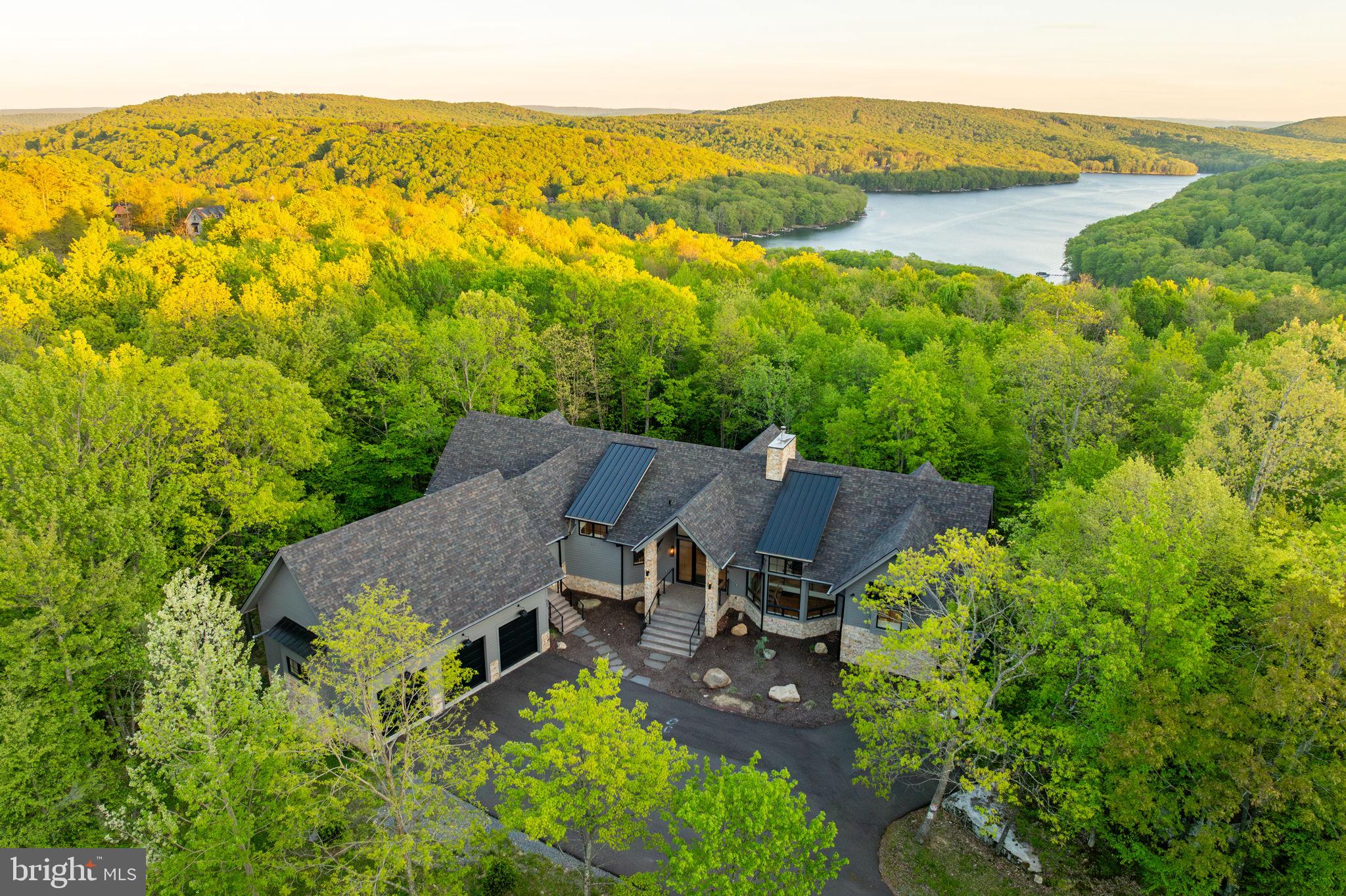 Welcome to Boulders Edge, a stunning mountain retreat perched above Deep Creek Lake, where luxury living meets the beauty of nature. Built in 2022 on 1.25 private acres, this exceptional home offers privacy, modern elegance, and panoramic lake and wooded views through floor-to-ceiling windows. Inside, you'll find soaring ceilings, a custom gas fireplace, and designer finishes throughout. The chef’s kitchen features a massive marble island, top-of-the-line JennAir appliances, a hidden prep kitchen, and sleek white oak cabinetry. The main level includes two spa-inspired primary suites, a dedicated office, and a stylish mudroom with custom gear storage. The expansive lower level is perfect for entertaining, complete with a full bar, game area, and a dramatic three-sided glass fireplace, plus three additional bedroom suites and bonus spaces. Step outside to a beautifully landscaped backyard with a hot tub, stone patio, fire pit, and a whimsical boulder cave. With a private, peaceful dock slip and easy access to year-round lake activities, Boulders Edge is the ultimate mountain getaway.