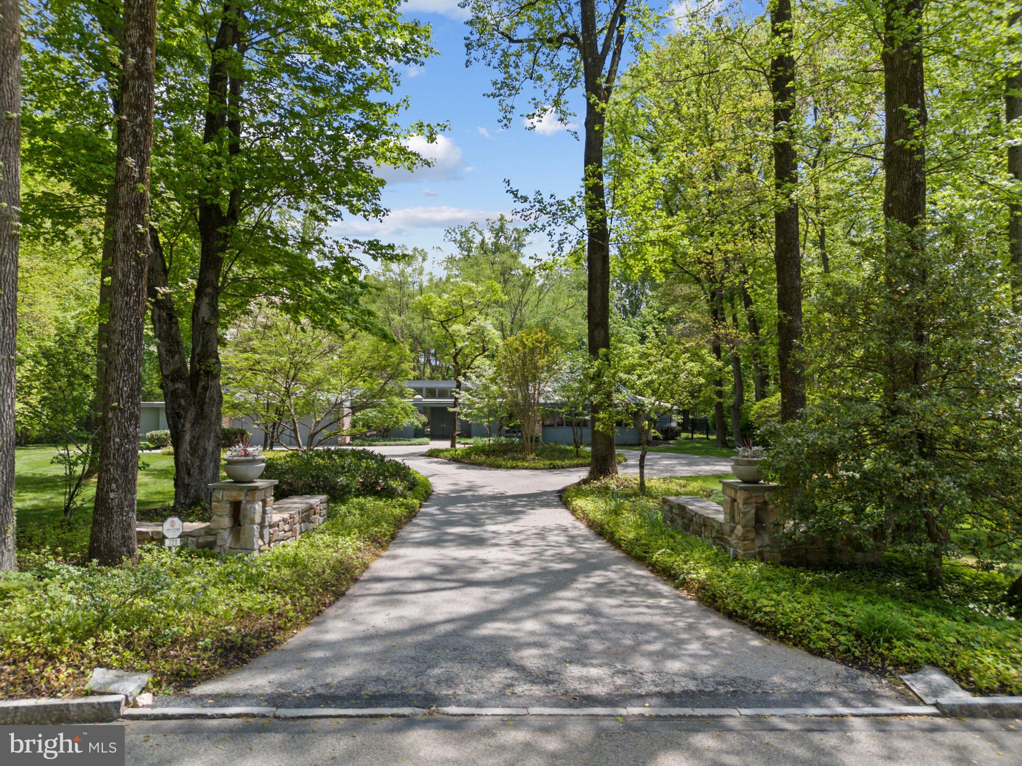 Welcome to 721 John Barry Drive, an elegant and expansive home nestled in the heart of prestigious Lower Merion Township. Set on a lush, meticulously maintained two-acre lot, this residence offers refined living inside and out—with beautifully landscaped grounds, resort-style amenities, and a layout ideal for both entertaining and everyday comfort. A gracious circular driveway welcomes you to this serene retreat framed by mature trees and specimen plantings.
Step inside to discover a bright and open floor plan accented by hardwood floors, recessed lighting, and thoughtful architectural details throughout. A wall of mirrored closets and a stylish powder room greet you at the entry. Just beyond, the sunken living room impresses with vaulted ceilings, a striking floor-to-ceiling stone fireplace, and expansive windows offering uninterrupted and breathtaking views of the scenic backyard.
To the left of the entry, a formal dining room flows seamlessly into the hallway and living areas and features a custom built-in table with seating for ten—plus additional leaves for expansion, making entertaining effortless.
At the heart of the home is a chef’s kitchen designed for both beauty and performance. Outfitted with granite countertops, a circular serving peninsula, abundant custom cabinetry, and high-end stainless appliances—including a six-burner Wolfe stove, Bosch dishwasher, Miele ovens, Whirlpool compactor, and Sub-Zero refrigerator—this kitchen meets every culinary need. A large main sink is complemented by a secondary prep sink, while the kitchen also offers direct access to the two-car garage and the backyard.
Adjacent to the kitchen, the light-filled family room features a second fireplace, skylights, and serene backyard views, with direct access to a screened-in porch for enjoying quiet mornings or warm summer evenings. A spacious office just off the family room offers built-in storage, a sink, and walkout access to the rear yard—ideal for remote work or creative pursuits. The lower level, accessed off the kitchen, provides abundant additional storage and room for future customization
One of several thoughtful additions to the home includes an expansive multipurpose room—once an art studio, now a flexible space that could serve as an enormous great room, gym, or game room, all with panoramic views of the backyard.
Through to the opposite wing of the kitchen, you’ll find a large pantry, a skylit laundry room, a storage closet, and an additional door to the driveway. A private fifth bedroom suite is located here—perfect for guests or multigenerational living.
Back at the front hall, turn right to discover a handsome wet bar alcove and a richly appointed library with a full wall of custom built-ins and pocket doors for added privacy.
The bedroom wing features the primary suite with generous customized closet space, shower and soaking tub and door to rear yard access.  Three additional ensuite bedrooms are positioned nearby, all designed to maintain privacy..
Step outside to a backyard oasis. The area between the house and the pool is elegantly hardscaped and accented by a cluster of River Birches, creating a tranquil transition to the resort-like amenities beyond. Enjoy a full-size tennis court, a sparkling swimming pool, and a well-equipped pool house complete with two full bathrooms, changing rooms, and a kitchenette—everything you need to entertain in style.
721 John Barry Drive offers a rare combination of luxury, flexibility, and natural beauty—all in one of the Main Line’s most coveted neighborhoods. This is a home that invites you to live expansively and comfortably, surrounded by timeless elegance and modern convenience.