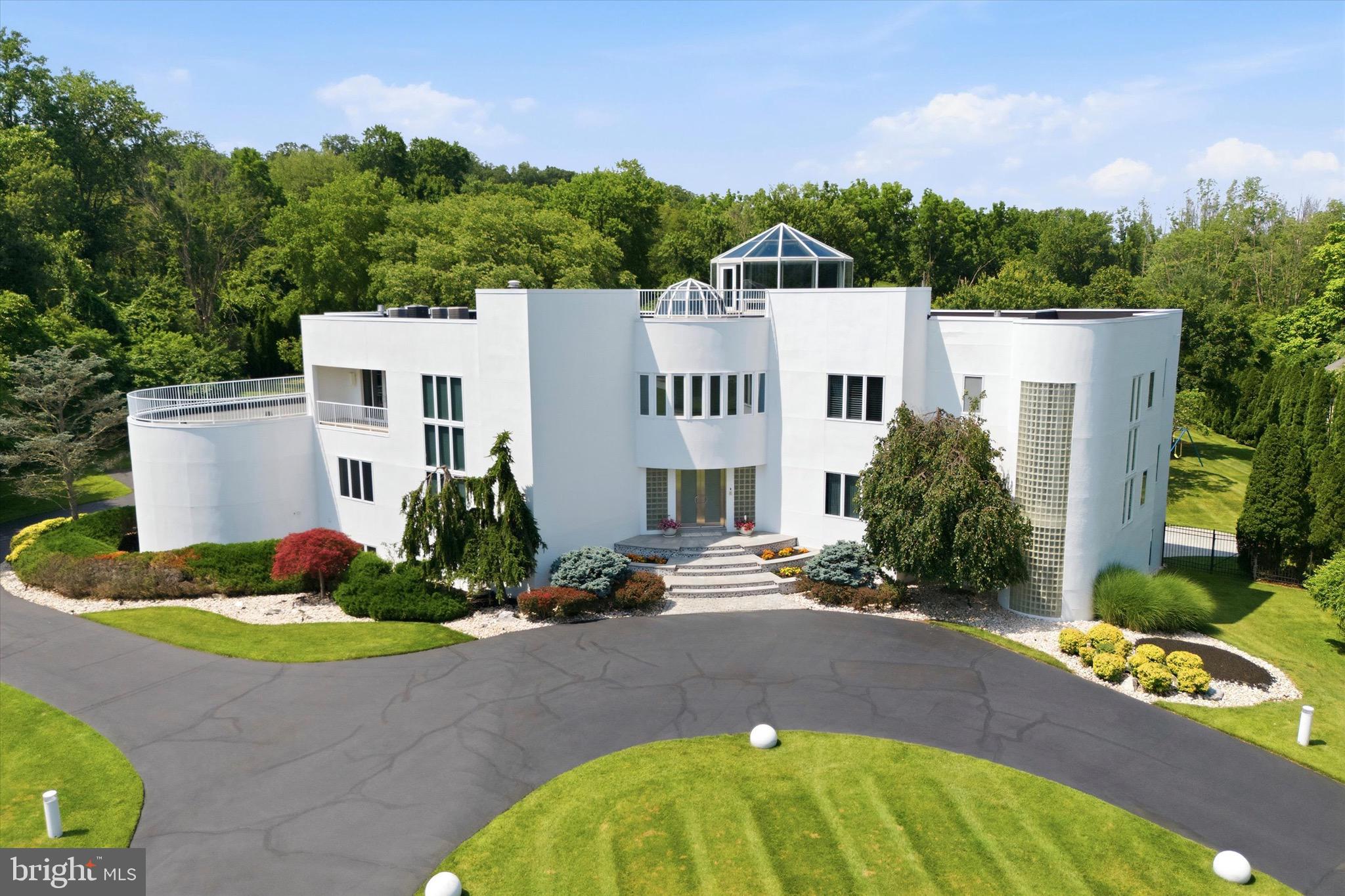 An architectural masterpiece of exceptional scale and timeless design, this extraordinary contemporary estate spans more than 13,000 square feet on 1.81 secluded acres, offering an unparalleled blend of modern elegance, privacy and resort-inspired living. Surrounded by mature trees and introduced by a sweeping circular drive, the residence is distinguished by its striking geometric architecture, dramatic curved walls, expansive glass and iconic rooftop observatory. A breathtaking two-story foyer with floating dual staircases, soaring ceilings and gleaming marble floors set the stage for interiors designed to impress while remaining effortlessly livable. Walls of glass flood the home with natural light, highlighting the home’s dramatic proportions and thoughtfully designed living spaces. The spectacular living room is a true architectural statement, featuring a distinctive sunken conversation area that creates an inviting focal point for entertaining. Formal and casual gathering spaces flow seamlessly through the home, offering the ideal setting for both intimate gatherings and large-scale entertaining. The gourmet kitchen is both functional and impressive, featuring custom cabinetry, premium appliances, an oversized center island and a unique built-in aquarium that serves as a stunning architectural centerpiece. Two main-level bedrooms with en-suite baths provide flexible accommodations for family and guests and an elevator to all floors ensures total accessibility. Upstairs, the luxurious primary suite is a private retreat, offering a large bedroom, spacious sitting room, fireplace, spa-inspired bathroom, a walk-in closet and access to outdoor terraces overlooking the grounds. A graceful curved staircase leads from the sitting room to the home’s spectacular glass-enclosed observatory—an inspiring space with panoramic views, offering a one-of-a-kind setting for working from home or quiet reflection. An adjacent office and four additional bedrooms with en-suite baths complete the second level. The finished walk-out lower level expands the home’s exceptional living and entertaining space with multiple areas for recreation, gaming and fitness, a bar, a bedroom, a full bath and direct access to the outdoor entertaining areas. Outside, the estate transforms into a private resort. Expansive terraces overlook the beautifully landscaped grounds, leading to a spectacular pool and spa surrounded by multiple entertaining areas. Bold contemporary architecture, exceptional craftsmanship, thoughtfully designed spaces and resort-caliber amenities combine to create one of the area’s most distinctive luxury residences. This is a rare opportunity to own an iconic estate where visionary design and sophisticated living come together to create an extraordinary experience.