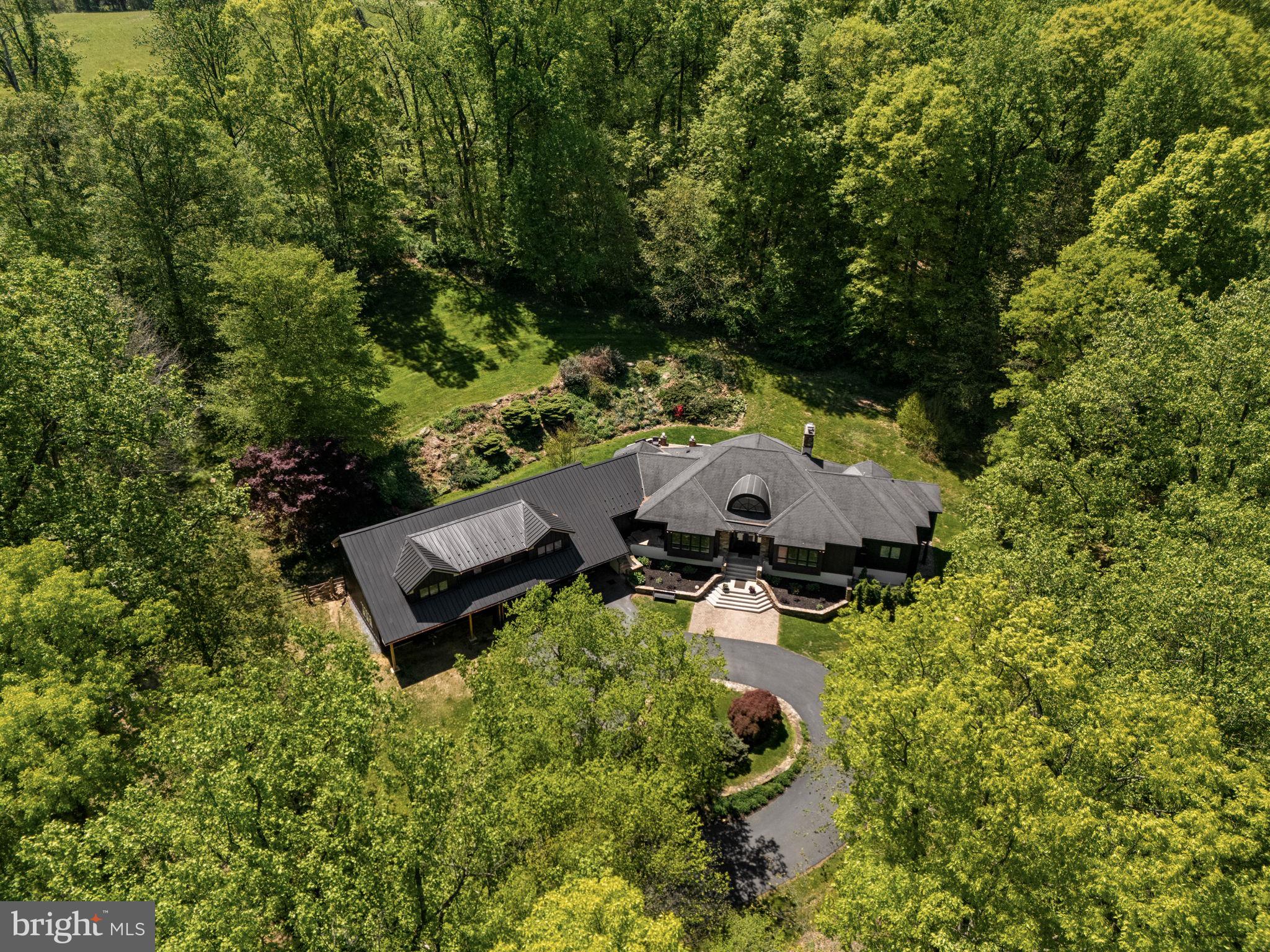 Some properties are simply a home. This one is something more, a rare opportunity for multi-generational living, a private homestead, or a flexible family estate, all wrapped into one extraordinary Chester County property.

Set at the very end of a long, semi-private approach, 2800 Horseshoe Trail reveals itself with quiet intention—where architecture, landscape, and privacy converge. A sweeping circular drive introduces the home’s striking exterior, newly finished in James Hardie board-and-batten siding with refined stone accents. Beyond, 8.5 acres unfold in a rare, uninterrupted expanse overlooking Birchrun Creek, creating a natural buffer of tranquility that feels worlds away.

Inside, the architecture becomes the experience. The dramatic octagonal Great Room anchors the home with soaring cathedral ceilings, a statement fireplace, and a full wall of windows that dissolve the boundary between indoors and the surrounding landscape. Light moves effortlessly through the space, highlighting custom built-ins and the home’s intentional design—crafted for both grand entertaining and quiet moments.

The primary suite is a private retreat in every sense—designed with a spa-level sensibility, featuring heated floors, a cast iron clawfoot tub, quartz surfaces, a window-lined walk-in shower, and a bespoke dressing area complete with walk-in and cedar closets. The kitchen balances beauty and function with quartz countertops, hardwood floors, a walk-in pantry, and a sunlit breakfast space that opens to a thoughtfully designed hardscape patio.

What truly sets this property apart is its rare ability to offer both connection and independence. The main residence flows seamlessly while providing distinct living zones, including additional bedrooms, a secondary living space, and its own laundry—creating flexibility without compromise.

A substantial, fully integrated addition expands the possibilities even further. Designed with intention and privacy, it features its own entrance, a kitchenette with custom cabinetry and quartz finishes, an open living area, a private bedroom suite, and multiple French doors that invite in natural light. Whether for extended family, long-term guests, or a live-in arrangement, it lives effortlessly as its own residence while remaining connected to the whole.

The lower level continues this theme of versatility, offering a finished retreat complete with a full bath, mirrored wet bar, lounge or fitness area, bedroom, and additional unfinished space with exterior access—ideal for evolving needs.

With approximately 7,500 square feet of living space, the home unfolds across multiple thoughtfully designed environments—four bedrooms, an office, den, multiple living areas, a kitchens and kitchenette, and layered indoor-outdoor living—all set within a landscape defined by privacy, natural beauty, and neighboring preserved land and equestrian estates.

This is more than a home.

It is a private estate—architecturally distinct, quietly luxurious, and designed for the way life is truly lived.