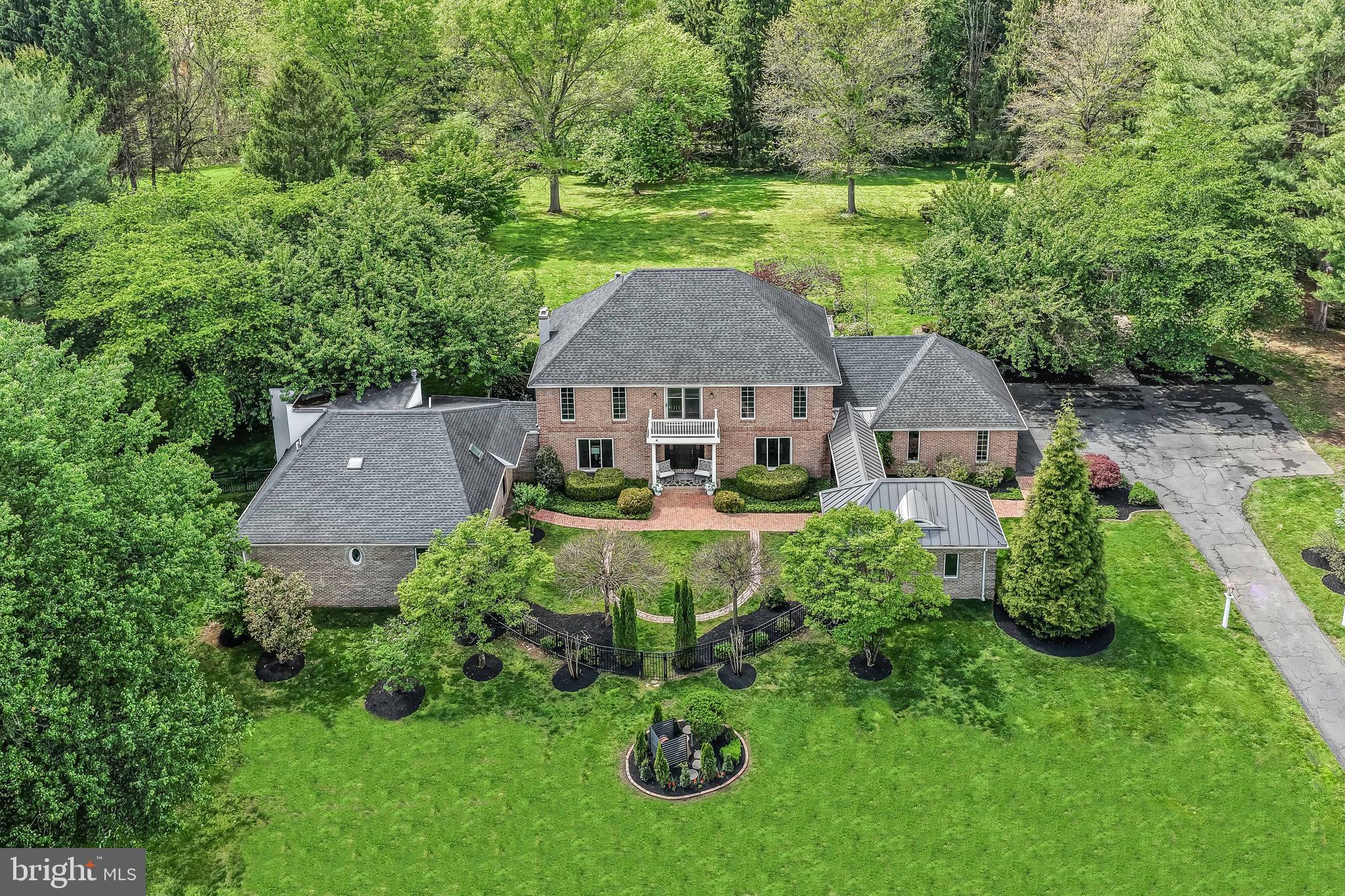 This elegant, fully custom, brick colonial home sits on a beautifully landscaped, flat, level, 2.4 acre lot that affords wonderful privacy. This special home has TWO PRIMARY BEDROOMS and TWO GARAGES, a separate DETACHED OFFICE, and a fully fenced garden area with a multitude of raised beds making this a wonderful home for multi-generational living, car enthusiasts, gardeners, and/or work from home professionals or artists.  The MAIN FLOOR PRIMARY bedroom was a fabulous addition, featuring a large bedroom suite with a private outdoor porch, vaulted ceiling , wall built-in gas fireplace, dressing room,  and large his and her's walk in closets. The main floor primary bathroom is not one, but actually TWO SEPARATE HIS AND HER'S FULL BATHROOMS, with luxurious finishes, skylights, decorative HEATED tile floors, custom shower,  and air jetted tub with a river stone floor and tub surround. Sliders from the bedroom open to a slate patio  overlooking the backyard,  perfect for quiet mornings or relaxing in the evenings. The remodel included the creation of a spacious laundry room with sink, custom tile work, tile floor, storage closet and sliding door to outside patio as well as the construction of a completely separate office building, complete with its own HVAC, fireplace, and eyebrow window plus the creation of a front entry courtyard with a brick walkway.  The front porch is oversized and the perfect place to sit and watch the dogs frolic in the fenced  in courtyard.   Once inside, you will appreciate the traditional center hall colonial layout with a formal living room and dining room on either side as well as the beautiful  hardwood floors throughout and the extensive mill work and gorgeous wainscotting. The chef's dream kitchen is just beyond the formal spaces and it features plenty of table space,  granite countertops, a stunning eat around kitchen island that runs the length of the kitchen, custom cherry cabinets, built in refrigerator, double sink, a Thermador 6 burner stove top, tumbled marble backsplash, Kitchenaid double oven and plenty of storage.   The kitchen is OPEN to the large family room which boasts a floor to ceiling brick fireplace and custom shelving/ built- ins which are perfect for displaying collectibles or storing those board games and books for family gatherings or peaceful reading. Beyond the kitchen and family room is a beautiful three season room with ceiling fan, wet bar with built in refrigerator and patios doors which open to the lovely terrace for easy entertaining or just a magnificent place to sit and take in all of the birds and wildlife that share this land with you.  The upper level has a SECOND PRIMARY BEDROOM complete with a large sitting area that has an outside entry to the lovely balcony overlooking the front courtyard, two walk in closets and a bath with a custom shower and double sinks. Three additional bedrooms and a hall bath complete the second floor.  The entertaining space continues in the finished basement which has a large open rec room area with a room-length full wet bar.  Adjacent to the rec room space is a charming hobby/craft room with loads of built in cabinets, storage and counter space and then plenty of space beyond in the unfinished area for storage or work room areas.  In addition to the attached 2 car garage, there is a separate, free-standing three car garage with a cupola.  The third garage is used for gardening and it opens to the fenced in garden area which features raised planting beds and a separate protected area for the fruits and vegetables that the birds and animals like to share. This meticulously maintained home is the perfect place for discriminating buyers to call home!