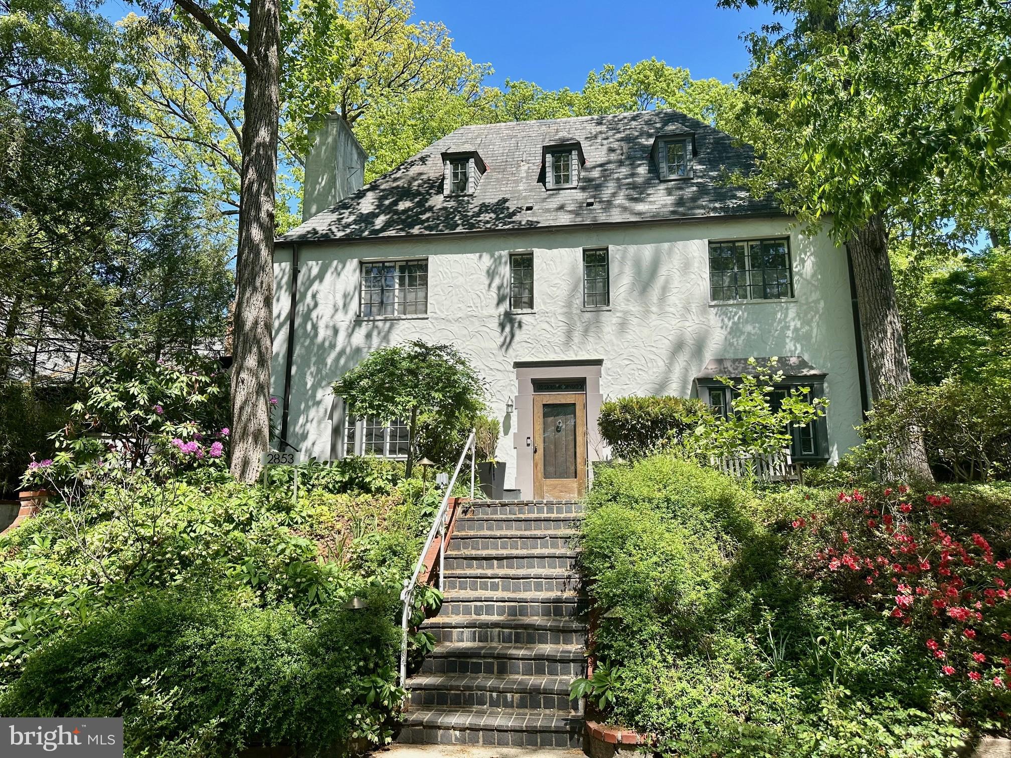 Tucked into the coveted enclave of Forest Hills on a private cul de sac, 2853 Allendale Place NW is a timeless 1928 stucco residence that blends classic architecture with thoughtful modern updates across four finished levels. Set on an expansive 8,529 square foot lot, the home is framed by a beautifully landscaped, private backyard with a lush garden and inviting outdoor living spaces.

A gracious foyer welcomes you inside, where the main level unfolds with a traditional living room anchored by a fireplace, a formal dining room, and a well-appointed gourmet kitchen featuring peninsula seating, ideal for both everyday living and entertaining. At the rear of the home, a stunning great room addition serves as the true heart of the house, offering table space, heated floors, a 2nd fireplace, remote-controlled skylights/shades, and dramatic soaring walls of glass that overlook the patio and serene backyard. A side den or office with powder room and access to the front balcony provides a perfect work-from-home retreat or quiet escape.

Upstairs, the second level hosts three generously sized bedrooms and two full baths, including a spacious primary suite with a walk-in closet and natural light enhanced by solar tubes. Fixed stairs lead to the top level, where two additional bedrooms await, one with its own en-suite full bath, offering flexible space for guests, family, or creative use.

The lower level is partially finished and includes a laundry area, a third full bath, ample storage, and direct access to the garage.

With its elegant proportions, unique architectural details, and exceptional indoor-outdoor connection, this special home offers both character and comfort in one of DC’s most desirable neighborhoods.