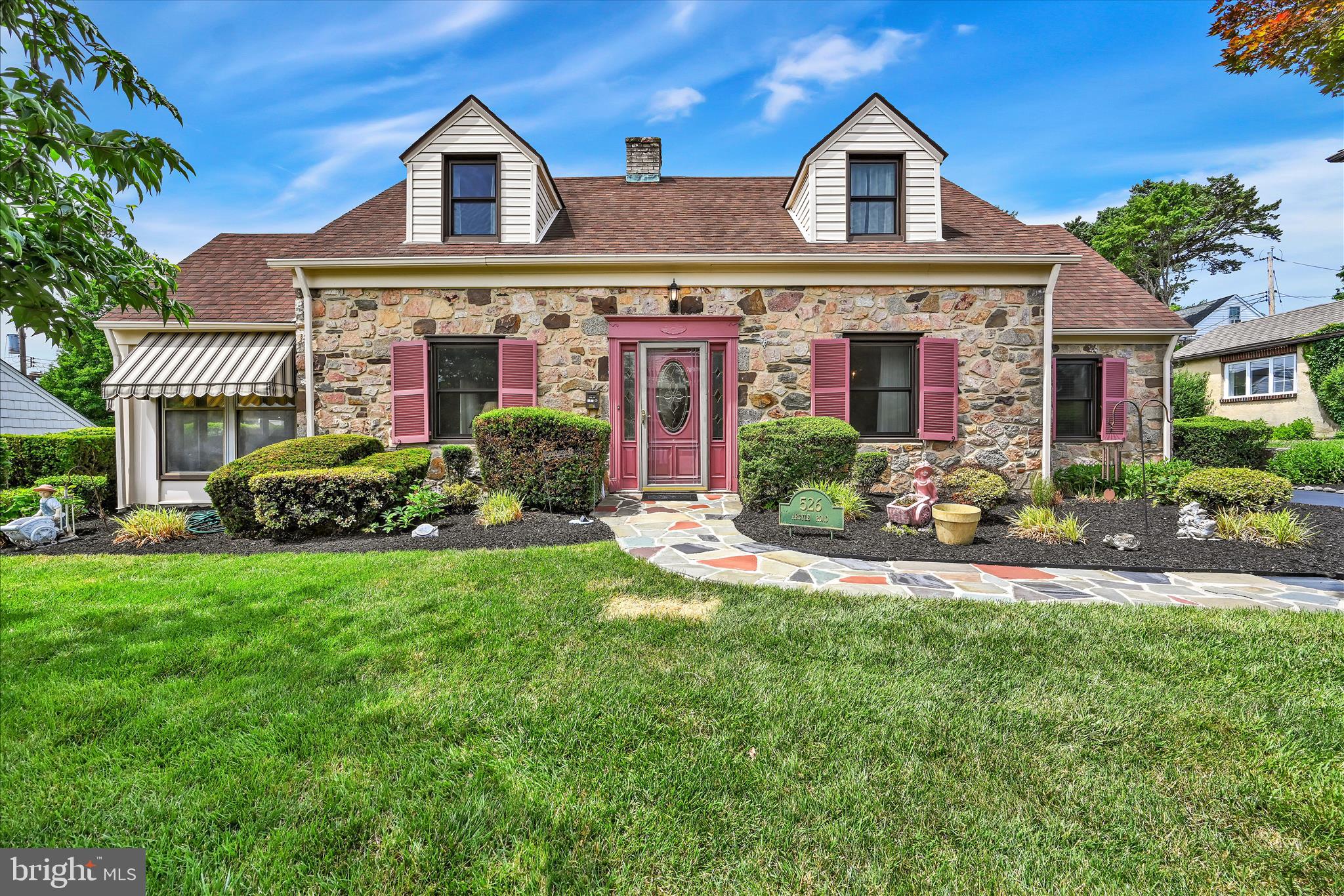 526 Argyle Road is a special place to call home, lovingly maintained and cared for by the current owner for 56 years. Only the second owner since its construction in 1943, this charming stone residence reflects decades of thoughtful care and showcases the enduring craftsmanship and character that are so difficult to find today. Located in the highly desirable Drexel Park neighborhood, residents enjoy holiday celebrations and community gatherings for all ages. This solid stone Cape Cod style home has been thoughtfully expanded over the years to offer multiple main level bonus spaces and a fully finished basement. The property is beautifully landscaped with mature, colorful plantings, while the newly sealed and expanded driveway provides ample off street parking. A flagstone walkway that was recently re-grouted and seal-coated, leads to the front door and enhances the home's curb appeal. Notable features include central air, gas forced hot air heat, a newer roof (approximately 2017), a kitchen expansion into the former garage area completed in 2001, 200 amp electrical service, and an HVAC system that is approximately 10 years old. According to the longtime owner, beautiful hardwood floors remain preserved beneath carpeting that has covered them for decades. From the moment you arrive, you'll appreciate the charm of both the home and its setting. Colorful trees and shrubs line the flagstone walkway leading to the front entrance. Inside, a welcoming foyer is flanked by a spacious formal living room with replacement windows and a fireplace, a bright main level sunroom, and a formal dining room. The kitchen offers Corian countertops, abundant cabinetry, and a pantry. In 2001, the owners further expanded the home by converting the garage into a 19 x 11 bonus room that flows seamlessly from the kitchen. This versatile space is ideal as a family room, playroom, television room, or additional dining area and features deep window sills, a ceiling fan, hardwood flooring and a 1200-watt baseboard electric heater. A convenient powder room and glass-paneled door, providing access to the level rear yard, complete the main level. The second floor offers three generously sized bedrooms, including a spacious 20 x 17 primary bedroom filled with natural light and featuring a neutral wall color and a ceiling fan. The hall bathroom includes a vanity and tub shower combination. A hallway linen closet and charming window bench provide additional storage and character.  The fully finished basement adds another level of living space and flexibility. Whether used as a home office, gym, playroom, or family room, this area offers endless possibilities. A French drain and sump pump provide added peace of mind.  The lot, measuring 84 x 100, is larger than many others in the neighborhood and offers a level backyard perfect for entertaining, gardening, or play.  The owner has gone to great lengths to maintain this home over the years, and it is now ready for its next chapter. 526 Argyle Road offers a wonderful opportunity to personalize a well loved home in one of Drexel Hill's most cherished neighborhoods.