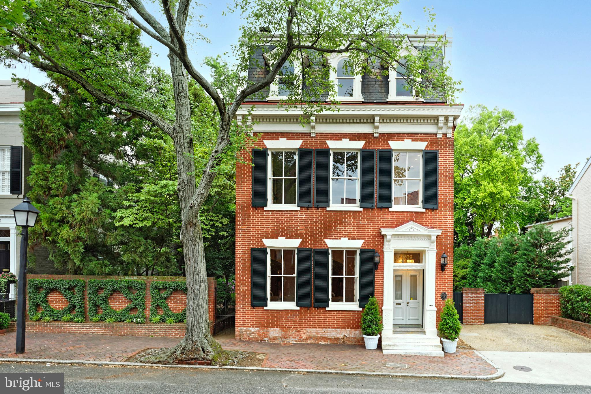 Gorgeous historic brick Federal-style townhouse in prime Old Town, Alexandria, built in 1812 and impeccably updated, expanded and restored! This freestanding jewel stands on one of the original 31 lots offered for sale in 1749, on a plat originally owned by Augustine Washington Jr., the half-brother of George Washington. Francis M. Hill purchased the property in 1884 and probably Victorianized the house including the Mansard roof. There have been many additional upgrades over the years such as the addition of a wonderful family room in 2011.

The stately home is enveloped by the south lawn and garden brimming with mature tall trees, azaleas, pink hydrangeas, boxwood, crape myrtle, and wisteria. In addition to its lush setting, the residence sits on a generous triple lot that includes an additional buildable lot and features classically elegant yet modernized interiors. Another amazing bonus is a rare converted carriage house in the rear, complete with its own private entrance, living space, full kitchen and skylight, making a perfect home office or artist studio; plus there’s a loft bedroom and bath upstairs for guest quarters, and French doors opening to the peaceful garden. 

Every inch of this important 6 bedroom, 4.5 bathroom house has been freshly painted, from all interior walls and doors to the exquisite millwork, extensive moldings and built-in bookshelves. Gracious living space is further enriched by stunning heart of pine floors throughout, 6 original fireplaces, cast iron radiators and other refined details. An inviting entry hall welcomes you, with wide arched openings to adjoining formal living and dining rooms that are well-suited for entertaining. Both are bathed in natural light, with wood-burning fireplace and matching mantles. Tall 11’ ceilings are found in the entry hall, living and dining rooms. Serve meals in the regal dining room with built-in storage and display shelves, then step out French doors to the garden terrace for coffee, after-dinner cocktails, and conversation.

The fabulous eat-in kitchen is appointed for the chef with custom cabinetry, huge granite-top island, stainless steel appliances including a Lacanche French range in an arched brick nook, and a sunny breakfast area with gas fireplace. Nearby is the glorious family room with striking coffered ceilings, a fireplace flanked by built-ins, 3 walls of glass, arched windows, radiant heat floors, and French doors on both sides to the outdoor oasis. A guest powder room, and convenient mudroom with heated tile floors, storage and laundry complete the main level.

The 2nd story also has airy 11’ ceilings, oversized windows on all sides, and several private retreats. A lovely sitting room/library with wood-burning fireplace, gorgeous paneling and built-ins is a peaceful place to read and lounge. Unwind in your divine primary bedroom with a relaxing fireplace and scenic garden views. Freshen up in the beautiful beadboard bath with an antique clawfoot tub, separate shower and original glass-front cabinet. There’s also a spacious dressing/sitting room with wall of closets, 2nd laundry area, and intimate guest suite with a cozy balcony and beautiful bath. Two more bright and comfortable bedrooms sharing a full bath await on the 3rd floor.

Three off-street parking spaces, and a premier location just a block from the shops and restaurants of King Street, and 2 blocks from the river take this gem over the top!