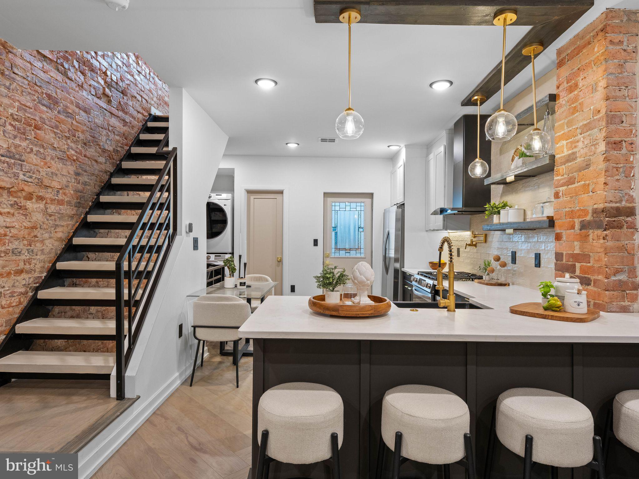 Welcome to 2339 S Bucknell St - a fully renovated 2 bedroom, 2 bathroom rowhome in the heart of South Philadelphia's desirable West Passyunk neighborhood. Thoughtfully redesigned with high-end finishes and modern industrial charm, this move-in ready rowhome offers the perfect blend of character, style and functionality. Step inside to an open straight-through layout featuring recessed lighting, exposed brick accents, custom wood beam details and designer finishes throughout. The show-stopping kitchen is complete with sleek two-tone cabinetry, quartz countertops, farm sink, floating shelves, gold hardware, a pot filler, stainless steel appliances and an oversized peninsula perfect for entertaining. Just off the kitchen, you'll walk out to your private multi-level back patio with Brazilian golden teak wood deck, white cedar shakers, and handmade live edge timber fencing for additional privacy. The spacious living and dining areas provide an inviting flow filled with natural light and carefully curated details that make the home feel warm and elevated. Upstairs, you'll find two comfortable bedrooms and a beautifully renovated bathroom featuring custom finishes throughout. The primary bedroom continues the home's unique character with handcrafted repurposed wood accents, while the spa-inspired bathroom makes a bold statement with exposed brick, wood paneling, black tile and elegant gold fixtures. A custom vanity with dual matte black vessel sinks adds a high-end designer touch, while the separate glass-enclosed shower stall and soaking tub create the perfect blend of luxury and functionality. The finished basement offers valuable additional living space with egress, making it ideal for a media room, home office, gym, third bedroom or flexible bonus living area. Located on a quiet South Philly block just minutes away from Passyunk Avenue, I-76, local restaurants, coffee shops, parks, public transportation, stadiums and Center City, this home delivers the perfect combination of convenience, lifestyle and one-of-a-kind design.