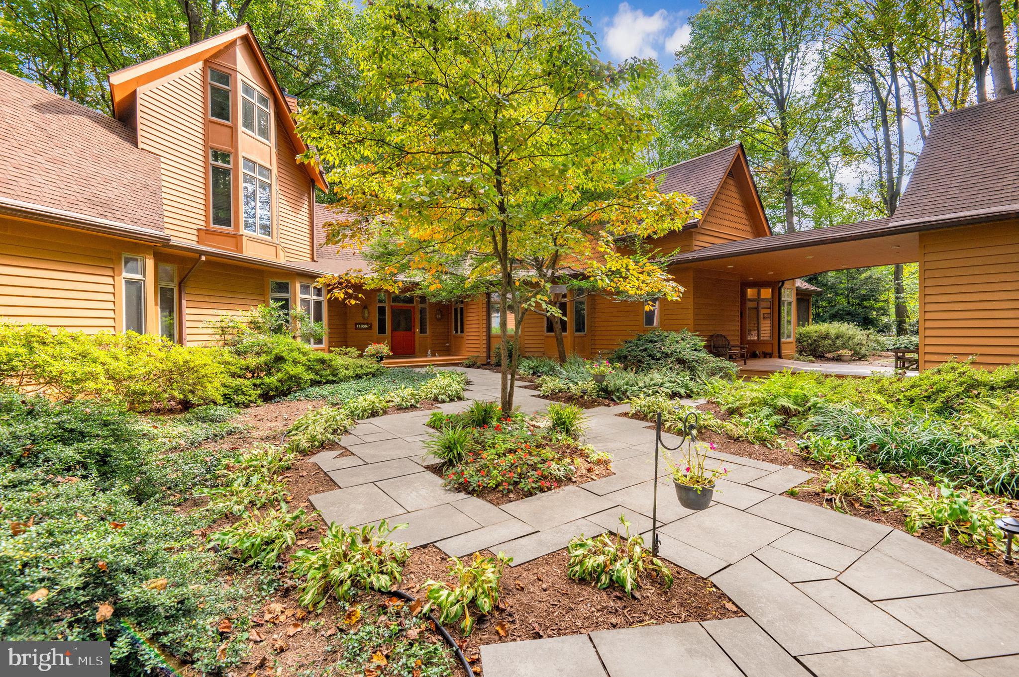Welcome to 11036 Dobbins Drive, a private retreat nestled on two and a half acres of meticulously landscaped gardens in Potomac, Maryland. This custom-built residence highlights four bedrooms, three and a half bathrooms over an impressive 5,100 square feet of living space. Designed with expansive open areas, bathed in natural light, and bedrooms thoughtfully placed on the main level, this property distinguishes itself as a unique and rare find in the Potomac area.

Journey along to the gated entrance, where an enchanting display of trees and gardens surround the circular driveway. The wood exterior and plethora of windows enveloping the home will instantly capture your attention. Follow the flagstone walkway to the covered front porch to enter the front of the home. A beautiful foyer with elevated ceilings and curved hallways greet you to take you to each main level offering. The windows throughout the home offer an immersive nature experience, blurring the lines between indoor comfort and the beauty of the outdoors. The sunken great room impresses with vaulted ceilings and panoramic wooded views through the oversized windows adorning the rear of the home. A wood burning fireplace takes center stage and access to the outdoor patio can be found through the glass doors. 

This residence is an entertainer's delight, boasting a magnificent dining room that effortlessly flows into the butler's pantry for seamless entertaining. Guests can savor the stunning garden views from the dining area, making every meal picturesque. The kitchen was tastefully designed with a spacious center island, ample cabinetry, a walk-in pantry, built-in shelving, and a cozy breakfast nook set against a bay window. For al fresco dining, step into the screened porch, equipped with a ceiling fan, which leads to the inviting wood deck. A practical mudroom is strategically located by the side entrance, equipped with a main level washer and dryer, while an adjacent room houses a built-in office area. A captivating library area lies further down the hall, featuring a wood-burning fireplace, surrounded by custom shelving and cabinetry. This space offers an idyllic setting for a work-from-home office. Additionally, the foyer is flanked by a discreet powder room and an oversized hall closet, ensuring storage for your everyday items. 

The main level graciously accommodates three bedrooms and two full bathrooms. The primary suite is a sanctuary of comfort, bathed in natural light from the surrounding windows that frame the private wooded views. Complete with built-in shelving and cabinetry, there is a space to store any item. The en-suite bathroom showcases dual vanities, walk-in shower, and an indulgent tub. A convenient vanity area connects to a generously sized walk-in closet, equipped with a built-in safe. Two additional bedrooms, wrapped in wooded views, complete this level, providing cozy retreats for family members or guests.

Ascend the hardwood staircase to the upper level, where you'll discover a distinctive loft area with vaulted ceilings and breathtaking treetop vistas. This versatile space serves as an additional living area, perfect for lounging while enjoying the scenic surroundings. A full bathroom and closet are located on this level, while a generously sized storage room offers space to stow away larger items.

Behind two wooden doors just off the main foyer lies a hidden gem - a staircase leading down to the unfinished lower level. As you descend, anticipation builds for the possibilities awaiting your creative touch. With its walk-out entrance to the backyard and generously sized windows letting in natural light, this space brims with potential. 

Outside, the beautifully landscaped lot unfolds with multiple gardens, a flagstone patio and deck providing a serene setting for outdoor gatherings and relaxation. This remarkable property is ideally situated, just minutes from Potomac Village, the Cabin John Shopping Center, and with easy access to bo