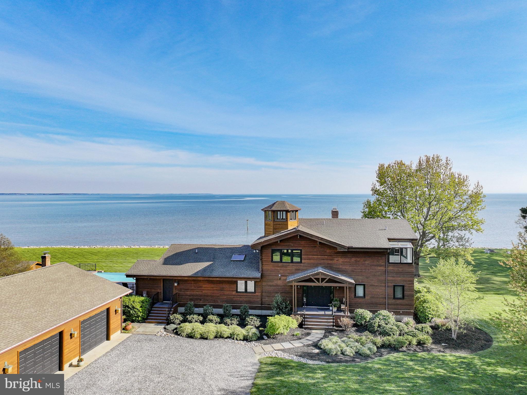 Welcome to your private waterfront retreat in charming Tilghman Island on over 5 acres of beautifully maintained property. The huge wraparound water views and broad open skies are equally inspiring. Uniquely situated at the base of the Island, this southern facing home looks across the mouth of the Choptank River and down the Chesapeake and for miles and miles. Find your tranquility in this tastefully updated one of a kind contemporary style cedar home with water views from every window. Lounge by the infinity pool, relax in the screened in porches, or drop your kayak in the open waters for a paddle around the Island.

Designed with an open floor plan and an abundance of natural light, this home features soaring ceilings in the living areas and a floor to ceiling hand crafted wood-burning stone fireplace. The updated gourmet kitchen, brightened by an overhead skylight, is complete with multiple work areas, a large center island with seating and an additional sitting area for keeping company while the chef is at work. The kitchen, dining and living space flow together to provide the perfect setting for everyday living and entertaining. Off the kitchen, a spacious laundry/mudroom with a utility sink and a front access door adds convenience and function. To complete the first floor there is one full and one half bath, both beautifully updated, a large bedroom facing the water with a screened in porch, as well as an additional lovely bedroom.

Upstairs, the loft provides a comfortable space for reading or watching TV and looks out over the great room with its wall of windows facing the water. From this room, climb the spiral stairway to the cupola to enjoy breathtaking 360 degree views. The sizeable primary bedroom features a vaulted ceiling and is brightened by a skylight and a row of water facing windows in the updated adjacent sitting area/office. The renovated en-suite marble bath has his and her vanities, a soaking tub, and a walk-in shower.

Improvements on the exterior of the house include an expansive composite board deck with beautiful aluminum railings, and a covered area perfect for hosting crab feasts. The two front porches have been similarly updated and are complemented by the newly stained exterior and extensive landscaping updates around the home. The oversized 4 car heated garage has new door openers and a large storage room with built in shelving. Behind the garage is a greenhouse and 8 raised garden beds for the vegetable garden enthusiasts. The private dock with a kayak lift has been resurfaced and is ready for you to check your crab pots and watch the sunset.