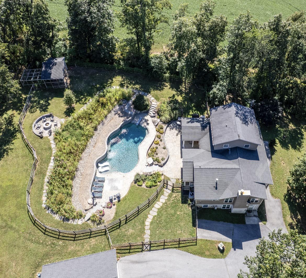 Incredible one of a kind estate! 5 bedroom 5 1/2 bath colonial style home with one of the nicest yards and pools in the area. The owners designed this home to entertain inside and out along with ease of living.  The main level has an open concept with recessed lighting throughout featuring a beautiful kitchen with stone counters, tiled flooring, large walk-in pantry, tiled splash and breakfast area that is open to the vaulted great room with wood flooring, kitchenette with stone counter and a tiled full bath. The kitchen is also open to  the cozy living room by a custom wood eating area and opens to a bright formal dining room along with a tiled half bath and a tiled mudroom to the rear yard/pool area. The main level also features the second primary bedroom with LVP flooring, walk-in closet with laundry and private tiled full bath. The upper level features the primary bedroom with LVP flooring, crown molding, private tiled full bath and private composite balcony. This level also has 2 other bedrooms, tiled hall full bath and a laundry area. The extensive lower level with recessed lighting throughout features a huge recreation room with high end fireplace wrapped in stone along with an exercise area, a media room with projector and movie screen, a custom home office with 3 work stations and built-in cabinetry, a full bath with marble flooring, a bedroom, laundry hookup and a utility area with storage. The exterior is absolutely amazing featuring a large covered patio with 2 ceiling fans, a composite rear covered porch, a huge composite covered front porch, large freeform patio backed by the stone retaining wall leading up the curving stone stairs to the custom heated saltwater pool complete with Pebble Tec finish, custom lighting, deep end with diving board, in pool lounging area, 3 waterfalls, hardscape and additional patio area. From the pool you can take the stone stairs on either side that both lead up to stone paths framing the wildflower meadow ending at the custom fire pit area. The owners have added fencing to isolate the pool area along with a side yard, small rear yard and large rear yard with vehicle gates. The oversized detached two car garage includes storage, electric and hides the pool equipment. There is an outbuilding that was used as a chicken coup the owner planned to convert to a pool house and storage along with a finished "tree house" with windows, locking door, futon and tv. The location is private and secluded offering trails through the wooded area in the rear however is only a short drive to the town of Manchester and offers easy commutes to Baltimore, Hanover PA, Westminster and many other locations. *****Aerial photos are from 09/2025*****