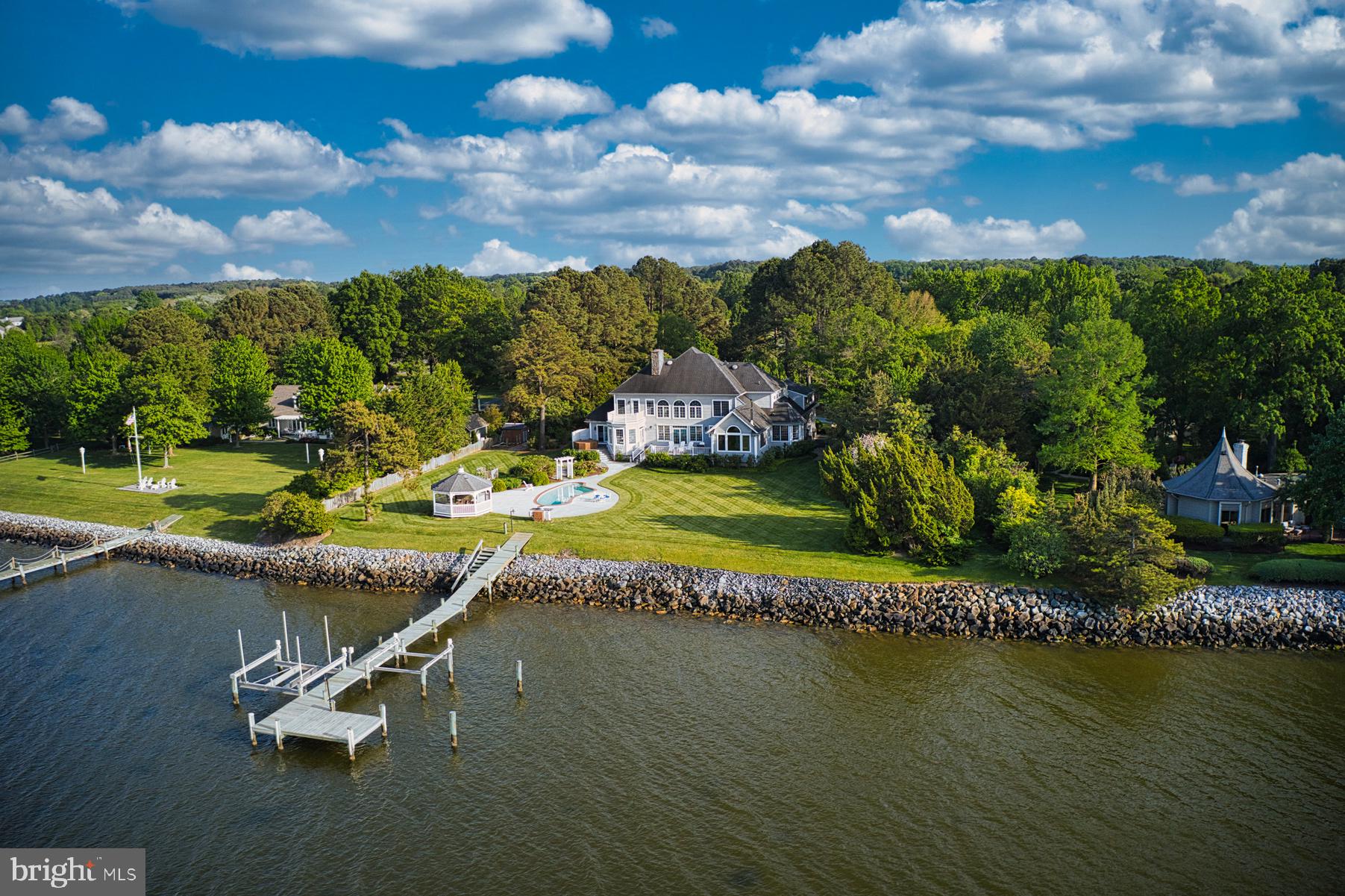 This property on a quiet three house cul-de-sac in the desirable Martingham neighborhood offers both close proximity to St. Michaels and breathtaking, panoramic and endless vistas of Porters Creek, Miles River, Wye River and the Eastern Bay by day and the sparkling lights of Kent Island Bridge at night. Sited high above a rip-rapped shoreline, the house’s rear wall is infilled with long windows and doors for maximum water views from most of the main rooms.

Enjoy the outdoors from elevated decks on the main floor living room and primary bedroom and the guest ensuite on the second floor, take a dip in the waterside pool, enjoy the hot tub or launch your boat from the either of the pier’s two boatlifts from an afternoon on the water. Relax afterwards in the spacious screened gazebo perched at the top of the shoreline for endless views.

The traditional style two-story house with abundant daylight from numerous windows, offers one-level living on the main floor including a sumptuous primary ensuite with a fireplace, living room with fireplace, dining room, study, open plan kitchen-breakfast room-family room, mud room and a three-car garage. Guest rooms and a bonus room are located on the second floor with a second stair to the main floor. One ensuite bedroom could also be a primary suite. The bonus room over the garage offers myriad possibilities including an artist studio, office or playroom. The basement level includes a spa area with a four-person sauna, fully equipped fitness room and storage.  as well as 2 bedrooms for overflow. The floor plan is zoned very well with easy flow among the rooms and the decks for relaxing with family and friends.

Amenities include flower gardens and a raised vegetable garden with shed, sprinkler system, public water and sewer plus a well for unlimited water supply, and broadband internet. No flood insurance is required due to the high elevation above the riprapped shoreline.

Move-in ready for you to enjoy the summer season!