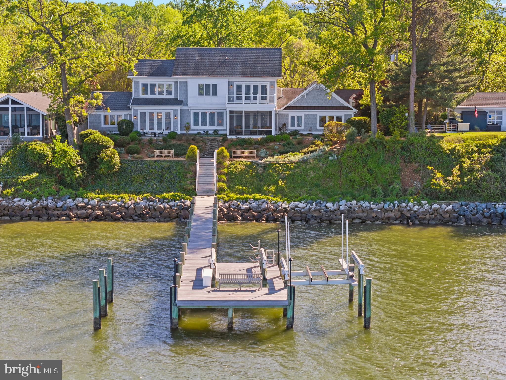 Commanding panoramic views of the Chesapeake Bay, Bay Bridge, and Eastern Shore, this exceptional waterfront residence offers an unparalleled waterfront lifestyle. The regions finest team was assembled including Purple Cherry Architects and Gate One Builders to create a custom masterpiece of style, design and tranquility.  Outside, a private 120’ IPE pier with two Hi-Tide boat lifts—including a 16K heavy-duty lift and a 6K lift for kayaks and jet skis—makes this a boater’s dream. Peaceful waterfront living is elevated with a screened IPE porch featuring breathtaking views of sunrises, sailboat races, and the Blue Angels. Inside, the chef’s kitchen is outfitted with a 55” Lacanche range, dual Bosch dishwashers, leathered marble countertops, Miele appliances, and a walk-in pantry. Reclaimed 150-year-old beams, an award-winning iron and bronze staircase by Maynard Studios and custom built-ins throughout the home reflect true craftsmanship. A main level secondary Primary suite with water views provides flexibility and convenience. Upstairs, the expansive primary suite offers serene bay views, a spa-style bath, dual closets, private library and balcony. Enjoy a glass of wine at the end of the day from the temperature controlled wine cellar in the lower level. An upstairs studio with a bay-facing balcony offers flexible living or guest space.  Timeless, thoughtfully designed, and meticulously maintained—2512 Lyon Drive is Chesapeake Bay living at its finest. Welcome Home!