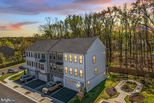 Better than new, this stunning end-unit luxury townhome showcases over $100K in premium upgrades and a sophisticated four-level modern design filled with natural light and upscale finishes throughout. This home offers exceptional energy efficiency with dual-zoned HVAC systems, a Rinnai tankless water heater, R-38 attic insulation, and durable brick & Hardie Plank siding. Elegant 7” engineered hardwood flooring extends throughout the home, enhancing its seamless, contemporary feel. The main level features 10-foot ceilings and an impressive open-concept gourmet kitchen designed for both everyday living and entertaining, complete with quartz countertops, waterfall island, pendant lighting, upgraded GE stainless steel appliances, custom soft-close cabinetry, designer backsplash, and range hood. The adjacent living area opens to an oversized Trex deck overlooking peaceful wooded views—perfect for relaxing or hosting guests. Upstairs, the luxurious primary suite offers a spa-inspired bath with walk-in shower, double vanity, and designer tile finishes, along with the convenience of a bedroom-level laundry room. The top-level loft and rooftop terrace provide the ultimate indoor-outdoor lifestyle, ideal for entertaining or enjoying sunset views. This level also features a private office with bath and wet bar, enhanced by large windows with expansive views—perfect for working from home or hosting guests. The lower level includes walk-out access to the backyard and direct entry to the garage, adding flexibility and convenience. Ideally located near top shopping, dining, and entertainment, with easy access to Route 28, Route 50, I-66, and Dulles International Airport, this home offers the perfect combination of luxury, location, and lifestyle. A rare opportunity to own a model-like end-unit townhome with rooftop terrace and premium upgrades—don’t miss it!