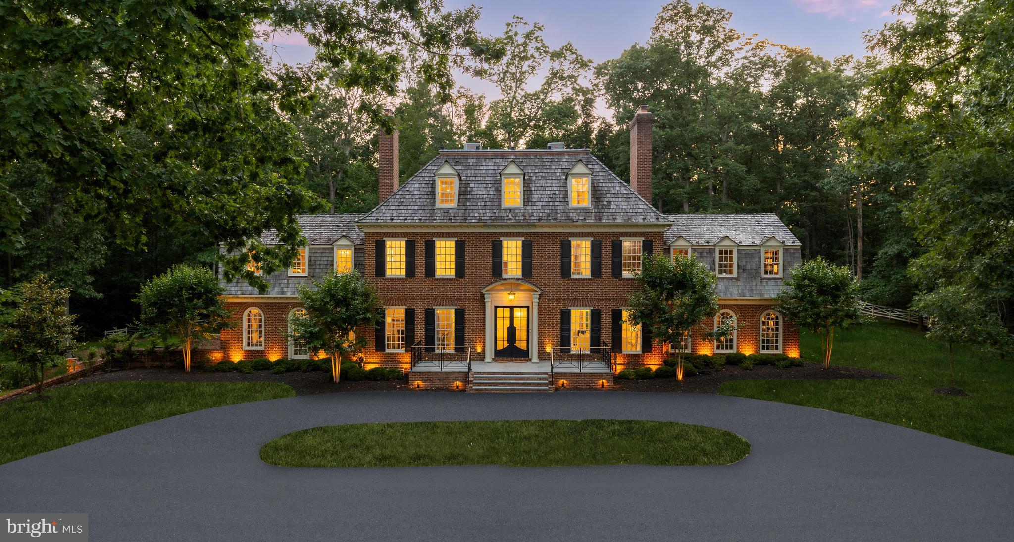 Manor Stone Drive is arguably one of the Capital Region’s best-kept secrets. Nestled along a wonderfully tranquil stretch of River Road adjacent to the Bretton Woods Club, it is a picturesque enclave of estate homes set deep into large wooded lots. 13300 is one of such homes, surrounded by white picket fences and mature foliage on five acres of land. With gardens designed by D.A. Dunlevy, the grounds, introduced by automatic gates, are a whimsical blend of sweeping vistas and towering trees. Originally constructed by master builder Patrick Cullinane, the property’s complete transformation is an homage to his exacting attention to detail and uncompromising penchant for quality. Its classically symmetrical, handmade red brick and restored wooden facade is a natural complement to the verdant backdrop. An expanded architectural front porch, featuring custom brass railings, creates a formidable first impression revealing a traditional center hall floor plan. The original wide plank hardwood floors have been restained to an elegant black, complementing intricate millwork which Cullinane’s artisans hand carved in each of his homes. Every aspect of the home is equally adept at hosting lavish gatherings as they are intimate daily life, from the formal dining room with its picture frame molding and roaring fireplace to the formal living room accessed through the builder’s famous archways to the cozy family room with its coffered ceiling and arched windows. Off the formal living room, a refined covered patio with marble floors, brick archways, recessed lighting, and designer chandeliers offers an elegant indoor-outdoor flow—perfect for seasonal entertaining or relaxing with lawn views. The highlight of the main level is arguably the soaring double-height library with spiral staircase, grand fireplace, and custom built-ins. Another is the show stopping Jack Rosen kitchen, whose exotic slabs of Brazilian quartzite are a feast for the eye alongside inset cabinetry and a hidden Thermador appliance package. The primary suite is noteworthy for its dual custom walk-in closets and sumptuous bath clad in contrasting black and white marble with heated floors, evoking images of the finest hotel suites, globally. It overlooks the rear of the home and features a private terrace, wood burning fireplace, and custom California Closets. Such premium touches throughout as Restoration Hardware fixtures, Emtek hardware, and custom Trustile interior doors are a testament to the no-expense-spared mentality when transforming the home. On the two upper levels, the five secondary bedrooms each have a luxurious ensuite bath and share conveniently located laundry facilities as well as a large open terrace overlooking the expansive lawn. The lower level, with its high ceilings, is an entertainment hub. Its floor plan revolves around a large recreation space, branching off into a fitness center with rubber flooring and accompanying full bath. The true professional home cinema is capped by a showstopping starlight ceiling similar to what is found in Rolls-Royce automobiles, and features state-of-the-art 4K projection and Dolby Atmos surround sound equipment. Systems upgrades include a smart energy management suite, intelligent HVAC, electric blinds, improved interior lighting, fully-redone plumbing and water treatment, and low voltage LED lighting around the property to create a radiant glow after the sun sets. Surrounded by five acres of flat, usable, green natural beauty, 13300 Manor Stone Drive is an elevated country estate providing a serene escape from the hustle of urban living.
