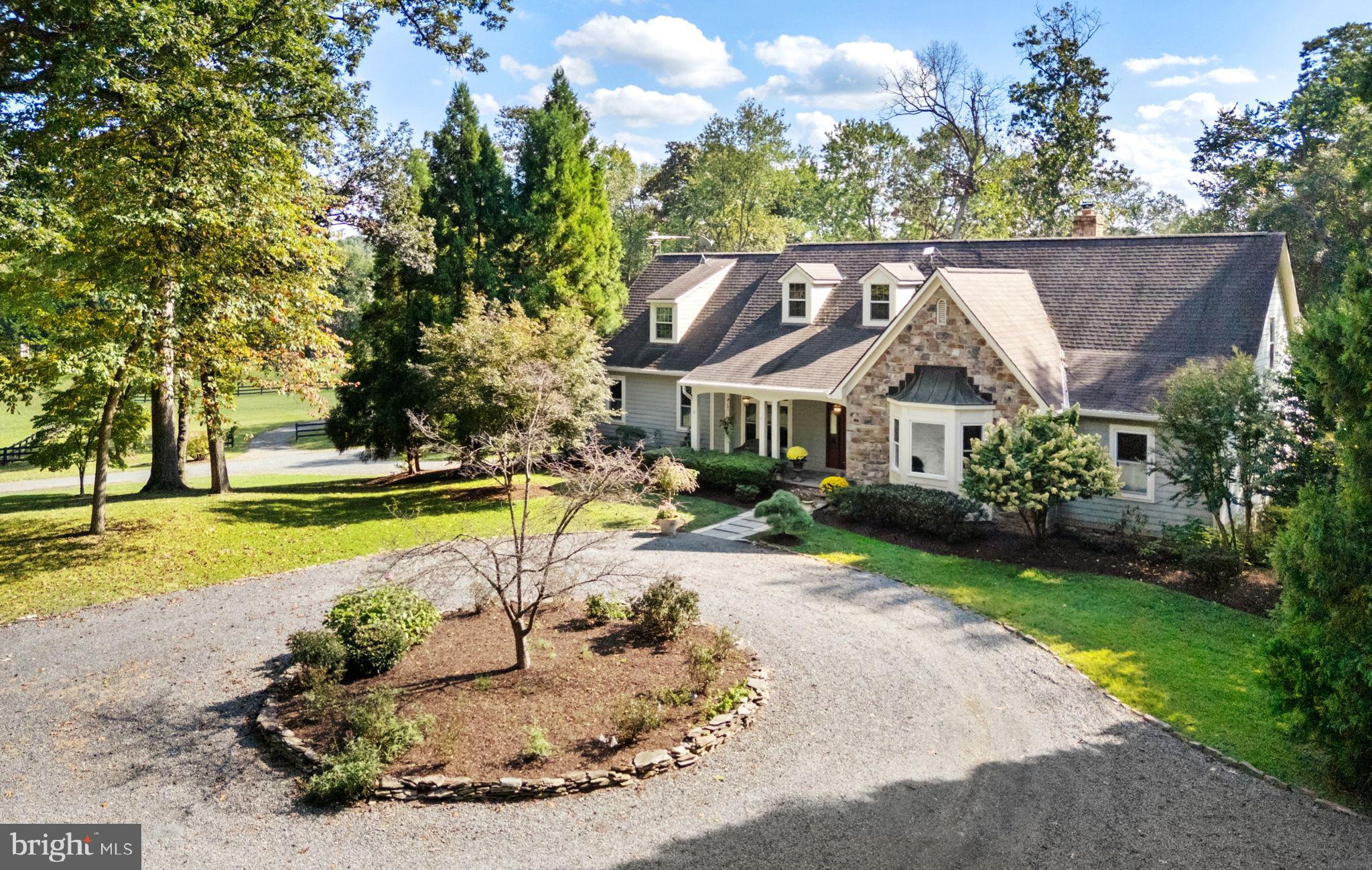 Welcome to White Oak Farm, a Southern Living–designed home tucked beneath towering oak trees on 12+ acres just minutes from Middleburg. Set back from the road the house enjoys both privacy and sweeping pastoral views. Quality built with Hardiplank siding and stone, the residence is complemented by a series of flagstone terraces that create inviting outdoor spaces for entertaining. Inside, the home is filled with warmth and character. Gleaming white oak floors, beams and bookcases were all milled from trees on the property. The heart of the home is the dramatic living room with its soaring 11+ foot ceilings, a floor-to-ceiling stone fireplace, and a wall of windows framing views of the covered porch and pastures beyond. The thoughtful floor plan blends formal and casual living. To one side of the foyer are two guest bedrooms sharing a Jack and Jill bath, while the private primary suite occupies its own wing, complete with a spacious walk-in closet, updated luxury bath with a 2-person walk-in shower, double vanities, and direct access to the rear terrace. Opposite the foyer lies the formal dining room and the expansive kitchen, anchored by a large island with cooktop and surrounded by custom cabinetry. A sunny breakfast bay, home office and laundry room adjoin this space with access to the 2-car garage below, back terraces and upper level. Upstairs is a 4th guest bedroom suite, a sitting room, and a recreation room. The outdoor living areas are just as inviting with multiple flagstone terraces that include a new outdoor kitchen area with built-in grill, a hot tub, and a stone chimney that creates the perfect gathering spot for cool evenings. For equestrians this farm is turnkey. A flagstone path leads to the 5-stall center aisle barn with a tack room, wash stall and feed room as well as overhangs on each side for hay and equipment storage. The barn area also includes a chicken pen and circular driveway for easy trailer access. Beyond are three fenced paddocks, two with run-in sheds, and a goat house with its own dedicated paddock. Toward the back of the farm is a footed riding ring and grass jumping field tucked against the woods. With its mix of open land and wooded privacy, this property offers both beauty and practicality. Recent upgrades include solar panels, new windows, Nest thermostats, Starlink and more. Located in Middleburg Hunt territory with excellent ride-out, White Oak Farm is a rare find. Don’t miss!