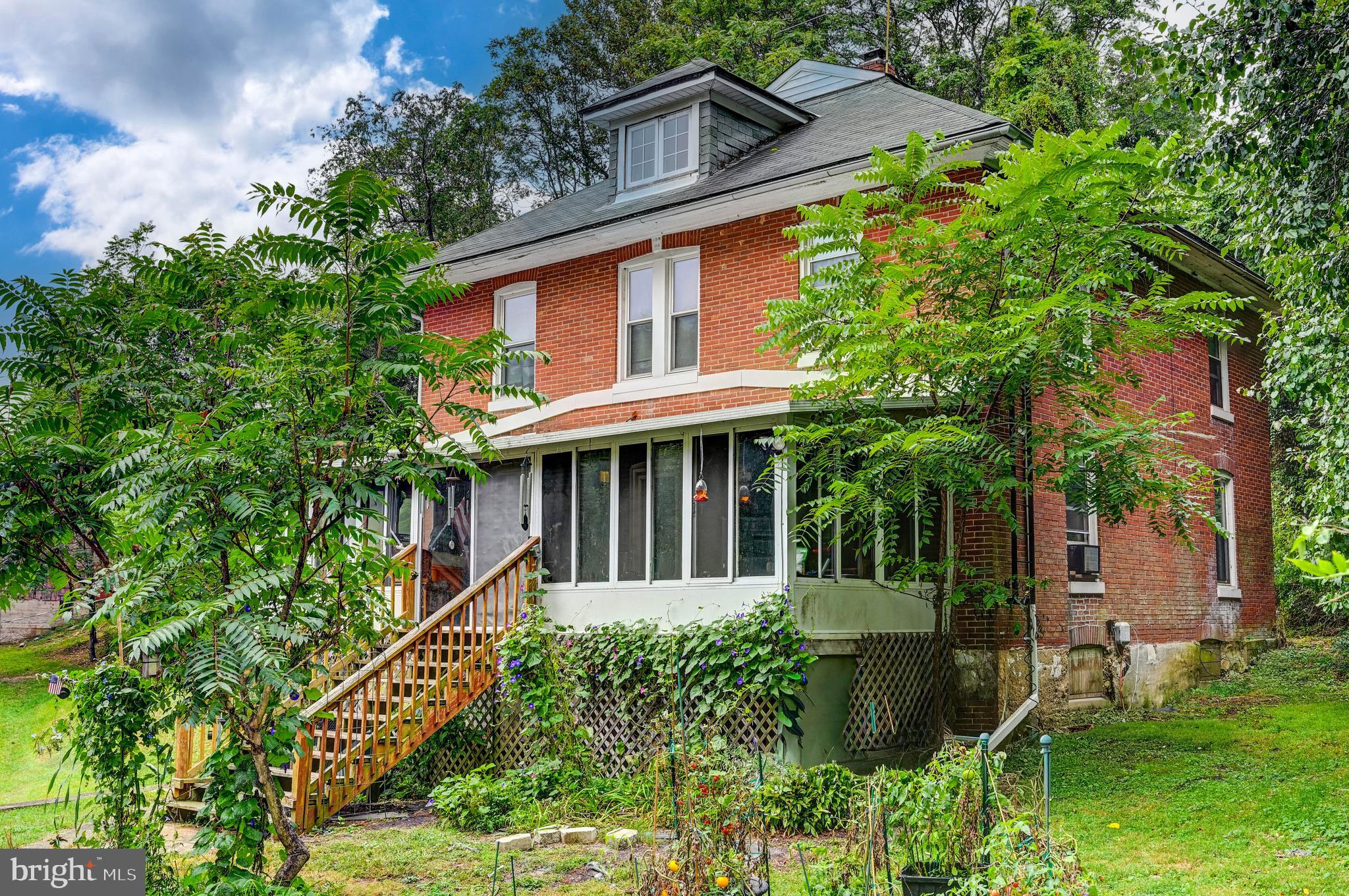Live authentically. Positioned on nearly five acres of mature greenery and natural privacy, this quintessential two-story brick Farmette carries the gentle romance of years past. Soaring trees and lush foliage frame the home, creating a natural sanctuary of privacy and calm. A grassy front yard and potted plantings lead to an enclosed porch that spans the façade... a perfect perch for taking in the pastoral views. Indoors, a dining nook invites lingering over simple pleasures, while the home itself radiates warmth, character, and a lived-in charm. A charming, classic red barn awaiting renewal. Endless potential... whether refined restoration or a visionary new build, an opportunity to imprint your aesthetic upon a true country retreat. Cultivate your existence. The art of uniting human and home.