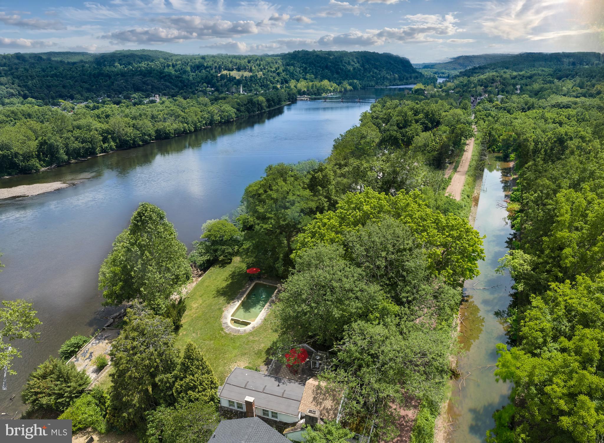 Less than a mile from the center of vibrant downtown New Hope is a river front home that feels like a world apart. It is set along the banks of the serene Delaware River and backs to the scenic Delaware Canal. Mature shade trees and expansive lawns frame this extraordinary property. Visitors are struck by the sweeping views. The home itself features three levels of living space with those exceptional views from nearly every window and door. A separate oversized two-car garage with storage room boasts a guest house above with full bath, kitchenette, and its own parking area. Old stone walls and a vintage well head add to the feeling of stepping back in time while bluestone paths and walkways, a roof deck and multiple patio spaces provide a wide array of outdoor locations to drink in the beauty of the river. At the river's edge is a large stone and timber terrace awaiting a new owner's updates - the possibilities are the stuff of dreams. In addition, there is a lovely in-ground cement pool with elegant halfcircle ends. With over .6 of an acre, extensive hardscaping and existing building footprint, one can only imagine what the future holds for this singular piece of paradise.