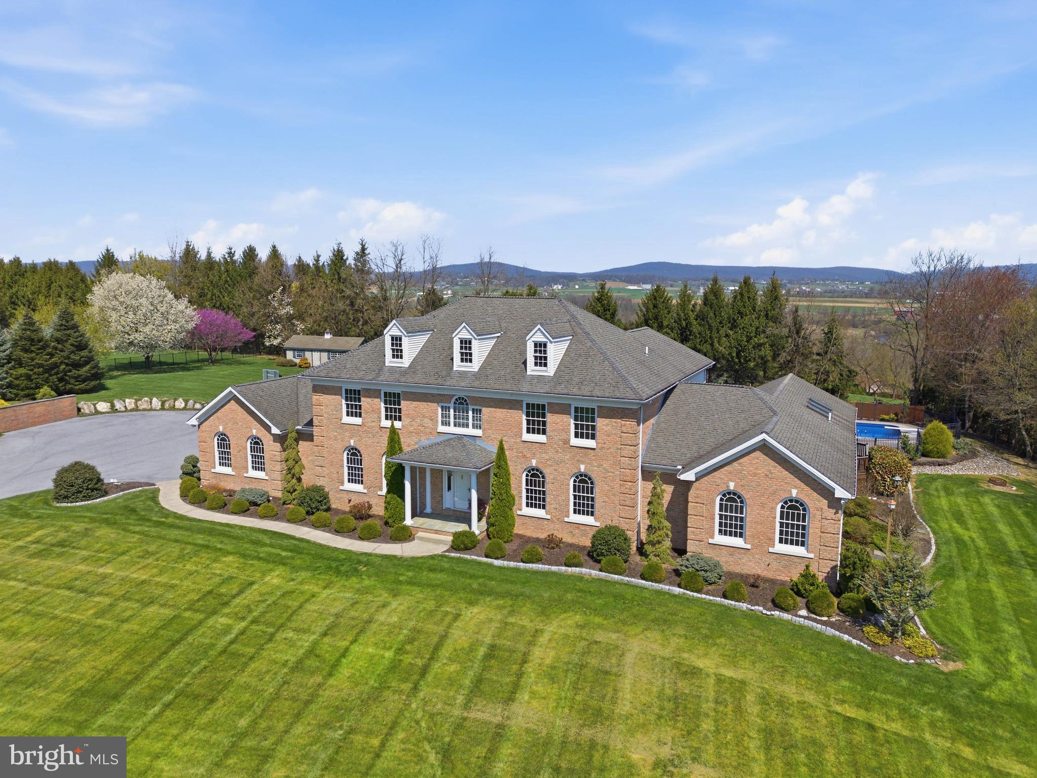 Welcome to 2 Breezy Knoll—an exceptional, custom-built builder’s home offering over 7 bedrooms, 4 full baths, and more than 8,000 square feet of finished living space on a private, elevated 3.9+ acre lot in the Warwick School District. Tucked away on a private road and set on a curated homesite with sweeping valley views on three sides, this architecturally driven Georgian Colonial delivers a rare blend of scale, craftsmanship, and privacy.

Inside, a grand two-story entry introduces an elegant and expansive layout highlighted by 9-foot ceilings, rich hardwood flooring, detailed millwork, and abundant natural light throughout. The main level features a formal dining room with crown molding and chair rail, a refined den with built-ins, and a spacious family room anchored by a striking gas fireplace with stone inlay and mantle. Overhead, soaring wood ceilings enhance the sense of scale and warmth, while expansive windows frame the surrounding landscape. A bright Florida/sunroom with skylights provides additional living space and tranquil views.

The gourmet kitchen is thoughtfully designed for both everyday living and entertaining, showcasing gorgeous granite countertops, cherry wood cabinetry, a large multi-level center island, walk-in pantry, and a sunlit breakfast nook. The kitchen flows seamlessly into the main living spaces, creating a natural gathering environment. A main-level guest bedroom with full bath, private office, and a convenient laundry/mud room with direct backyard access add flexibility and function. Additional features such as central vacuum and integrated security with exterior cameras enhance everyday convenience.

Upstairs, the spacious primary suite serves as a true retreat, complete with a walk-in closet and a luxurious en-suite bath featuring a jetted tub and walk-in shower. Four additional bedrooms provide generous accommodations, while a well-appointed full bath with integrated laundry adds everyday practicality. A private upper-level office—accessed through the primary suite—offers a quiet, dedicated workspace.

The finished lower level significantly expands the home’s versatility, offering a wet bar and kitchenette, a large recreation and game area, additional bedroom and full bath, exercise room, and extensive storage and utility spaces. With windows for natural light and direct access to both the interior and garage, this level is ideal for entertaining or extended living arrangements.

Outdoor living is equally impressive, featuring a covered rear deck with a wood-framed canopy overlooking the private grounds. A large in-ground saltwater pool—complete with a diving board and basketball hoop—is surrounded by an expansive paver patio, creating a resort-style setting for relaxation and entertaining. The professionally landscaped backyard offers ample room for gardening and recreation, along with a large, well-equipped shed on a concrete slab with electric service, providing exceptional storage or workshop potential. The lot itself backs to trees and offers incredible scenic vistas, enhancing the peaceful atmosphere.

Additional highlights include a 3-car oversized garage, expansive driveway parking, EV charging capability, and numerous recent improvements and system updates that reflect pride of ownership throughout. Located just minutes from Lititz, Lancaster, and major routes, this property presents a rare opportunity to own a truly distinctive estate in a private, picturesque setting. Schedule your private showing today!