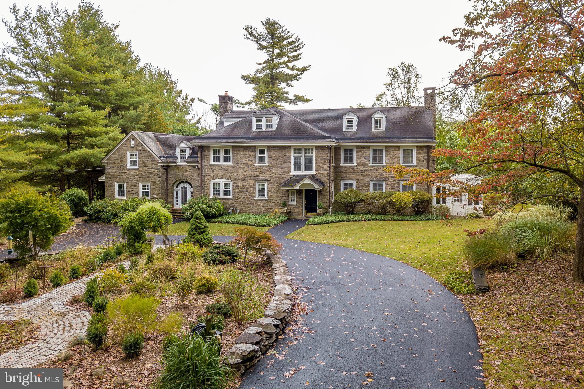Welcome to 123 Gypsy Lane, a stately 6-bedroom, 5.5-bath Georgian stone estate in Gulph Mills, offering timeless elegance and exceptional space on 2.5 private acres. Built in the 1920s, this grand residence combines classic architectural charm with the comfort and versatility today’s lifestyle demands. The entry foyer sets the tone with hardwood floors and original crown molding, leading to a powder room conveniently located near the front door. Towards the back of the foyer, you have an arched doorway leading to a sitting room with direct access to the back patio. To the right, the formal living room showcases hardwood floors, crown molding, a brick wood-burning fireplace, and French doors on either side opening to the sunroom, where slate floors and warm wood paneling create an inviting retreat with access to the patio and yard. To the left of the foyer, the library exudes sophistication with hardwood floors, crown molding, built-in bookshelves, a ceiling fan, and a second brick fireplace. The formal dining room features hardwood flooring, crown molding, chair rail detailing, built-in cabinetry, and French doors leading to the patio, offering seamless flow for entertaining. The kitchen includes tile floors, a butler’s pantry, stainless steel appliances, a double sink, and ample cabinetry, while the adjacent breakfast room with hardwood floors provides a cozy space for everyday meals. Upstairs, the second level hosts six spacious bedrooms, each with hardwood floors, ceiling fans, and access to a private bathroom for each bedroom. The third floor features a finished attic space—perfect for a playroom, home office, studio, or additional living area. The lower level basement has the home’s utilities, a laundry area with washer, dryer, and utility sink, and ample space for storage or future expansion. Outside, the 2.5-acre lot offers serene privacy, mature landscaping, and a slate patio ideal for outdoor entertaining or quiet relaxation. This extraordinary home is ideally located across from the Gulph Mills Golf Club, near the King of Prussia Mall, The Overlook at King of Prussia, major routes including I-76, and within walking distance to the Gulph Mills train station. With its combination of grand architecture, functional layout, and unbeatable location, 123 Gypsy Lane stands as a true showcase of refined living in Gulph Mills.