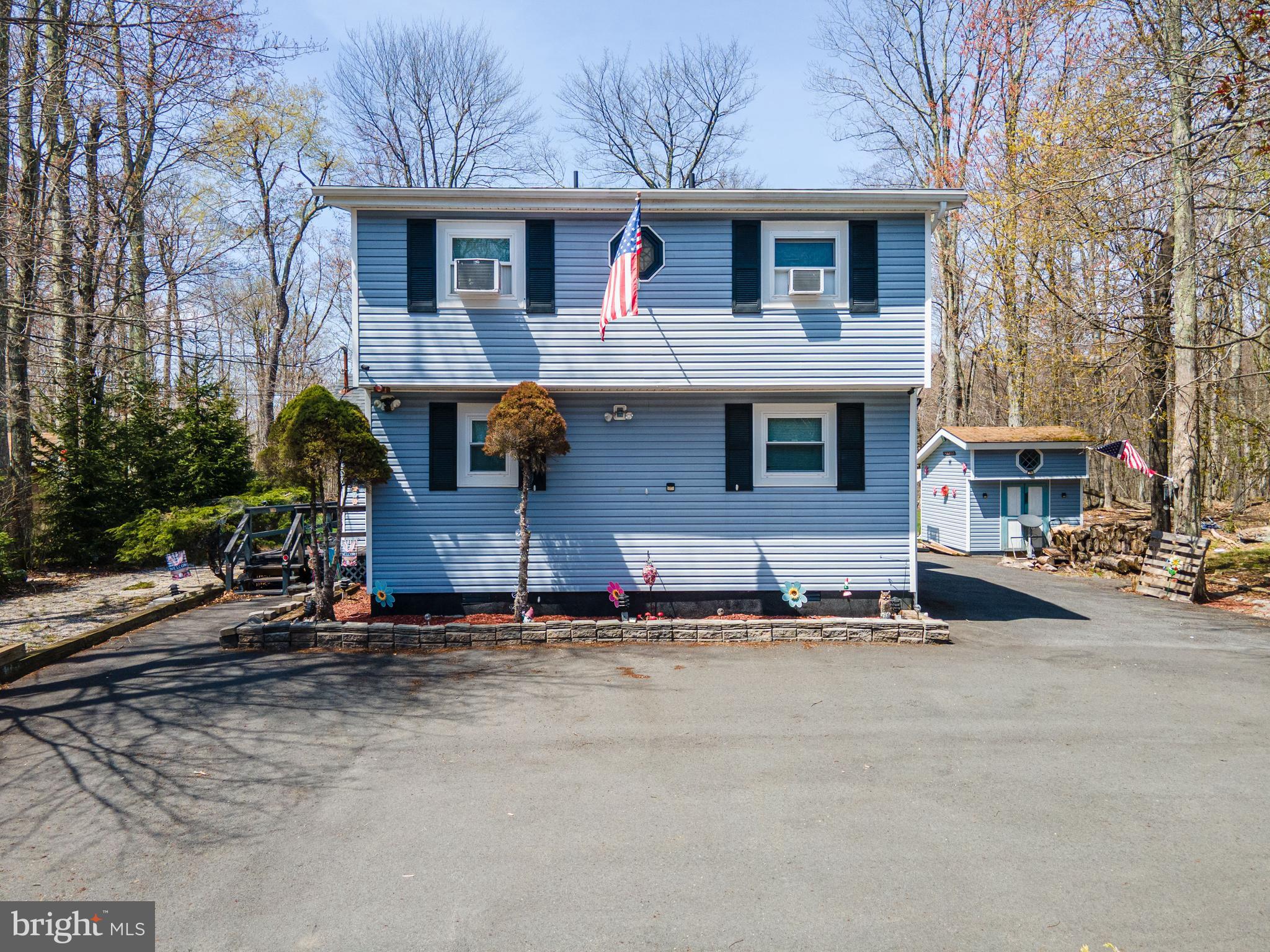 Tucked away in the scenic Pocono Mountains, this charming 2-bedroom, 2-bath contemporary home with a full vinyl facade offers comfort, character, and privacy. A large wraparound paved driveway begins at the front and extends around three sides of the home, providing ample parking for guests. Inside, wall-to-wall carpet flows throughout the open-concept family and dining rooms, highlighted by a vaulted ceiling with skylights and a ceiling fan. The family room features striking floor-to-ceiling wood-paneled walls and a stone fireplace with mantel, creating a warm and inviting atmosphere. The bright dining area includes sliding door access to a walkout deck—perfect for relaxing during long summer evenings surrounded by lush trees. The open kitchen is equipped with stainless steel appliances and sink, recessed lighting, a ceiling fan, and a convenient breakfast peninsula. The first-floor bedroom offers wall-to-wall carpet and easy access to a full bath with luxury vinyl plank flooring and a tub/shower combo. Upstairs, a finished loft provides a versatile space ideal for an office or sitting area with views overlooking the family room. An additional bedroom with a vaulted ceiling, wall-to-wall carpet, and dual closets, along with a full bath featuring luxury vinyl plank floors, tub/shower combo, and linen closet, completes this inviting home. Conveniently located close to major highways I-80, I-380 and I-84 for easy commute, Camelback Ski Resort, K Pool, Dresser Lake Park, Pocono Farms Country Club Association, shops, restaurants and so much more! *ALL FURNITURE & BELONGINGS INCLUDED IN THE SALE*