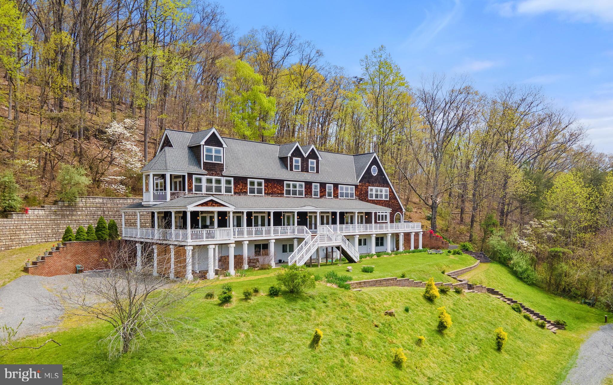 The residence at Groundhog Hill was conceived as a country retreat modeled on the stately shingle style summer homes of the Northeast.  The house takes advantage of the private setting and the distant mountain views.  The grand home in a rustic setting is a stunning combination.   While patterned after houses from the turn of the last century, Groundhog Hill provides a comfortable 21st century perch from which to explore the wild landscape of this private valley.

The residence at Groundhog Hill was designed as a gathering place for family and friends.   In addition to the large living room, library/den, and dining room, there is also a downstairs media room and finished attic rooms for more informal gatherings.   On three of the four floors are bedrooms or bedroom suites, that, depending on configuration, can provide overnight accommodations with anywhere from 7 to 9 bedrooms.  Spanning the entire length of the house is a grand porch which offers plenty of places to sit, dine, or just watch the mountain views.   A terrace below the porch offers the same space at ground level.  More intimate outdoor areas include a balcony off of the master bedroom and a side garden next to the mud room/Kitchen entrance.

Despite its large size, the house offers intimate spaces throughout.  Cozy reading nooks, side rooms off of bedroom suites, and built-in bookshelves and seating provide escapes from the larger entertaining spaces.   The interior space very much takes its cue from the rambling summer homes of the Edwardian era and care has been taken to source door hardware and lighting fixtures that reflect that time period and the house architecture.   Yet modern touches such as an elevator, sound system, bar fridge, and a gourmet kitchen are all seamlessly combined with period fittings.

Groundhog Hill is nestled in a hollow surrounded by the hills and mountains of the Blue Ridge.  Indeed, the bulk of Utz Mountain forms the southwestern corner of the property.    Most of the property is wooded with fairly mature hardwoods and a few pine and includes an abundance of native flowering trees and shrubs such as dogwood, redbud, and mountain laurel.  There is considerable timber value in the larger trees, but the mature canopy provides a relatively open understory on the hillsides for hiking trails.  There are several well draining an nicely sloped hillsides suitable for planting a vineyard.  Two bold streams course through the property and eventually merge, creating an ideal location for a pond.  One of these creates a boundary between the wooded upland and the open fields/meadows of the property entrance and main drive.   Of the 192.6 acres, in four tax parcels, only approximately 60 are open land.  These open fields are currently unfenced and kept in hay.  But they can be easily expanded to include more acreage and fenced for any type of livestock.  There is a woven wire property perimeter fence   A farm track veers off the main drive and follows along a stream to a large metal framed barn that can be used for equipment or hay storage, or converted to livestock use.  There are several outstanding building sites on the property for additional dwellings with private settings and mountain views.

Nearer the house are sloping lawns and planted retaining walls that frame the residence and provide overflow parking for bigger events.  These areas are landscaped with a variety of smaller trees and shrubs.
