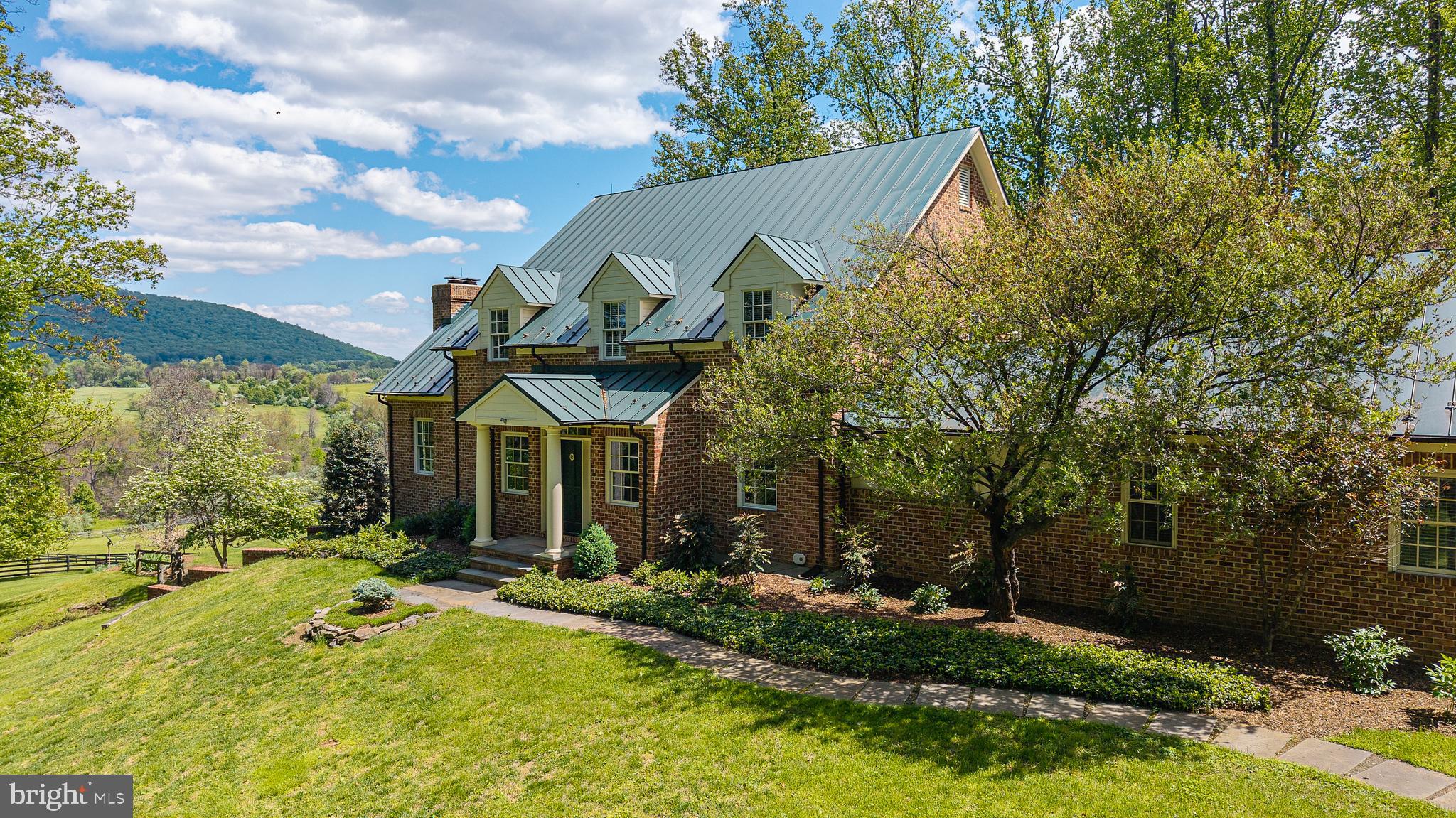 Tucked away at the end of a quiet private drive, this exceptional 21.51-acre property offers a rare blend of natural beauty and refined living. Enjoy sweeping, unobstructed views of Big Cobbler Mountain as you overlook thousands of acres protected by conservation easement—ensuring your vista remains forever unspoiled. A gentle stream meanders through the land, feeding into Thumb Run along the eastern boundary, while portions of the acreage benefit from land-use status for seasonal cattle grazing. The property is two separate tax parcels, offering flexibility and long-term value.
This elegant three-level Hunt Country style  residence offers timeless craftsmanship and modern comfort. Features include four spacious bedrooms and four-and-a-half baths, with approximately 3,800 square feet across the main and upper levels, plus an additional 1,500 square feet of beautifully finished walk-out basement space. French doors in the primary suite and dining room open to beautiful gardens. 
Exquisite custom detailing throughout, including oversized crown moldings, finely crafted window and door casings, and impressive 8-inch baseboards—hallmarks of true quality construction.
The home’s exterior showcases antique brick paired with durable fiber cement siding, complemented by a standing seam metal roof. Copper half-round gutters with leaf filters add both elegance and functionality. High-performance Pella windows and doors, along with 2x6 exterior wall construction, enhance energy efficiency year-round. Board fenced paddock and fields  with automatic waterers. 
Also included is additional detached garage building with workshop and loft, with plenty of room for equipment storage, firewood storage, together with two additional sheds. 
Welcome to a rare blend of refined living and thoughtfully designed outdoor spaces — where comfort, craftsmanship, and functionality come together in perfect balance.