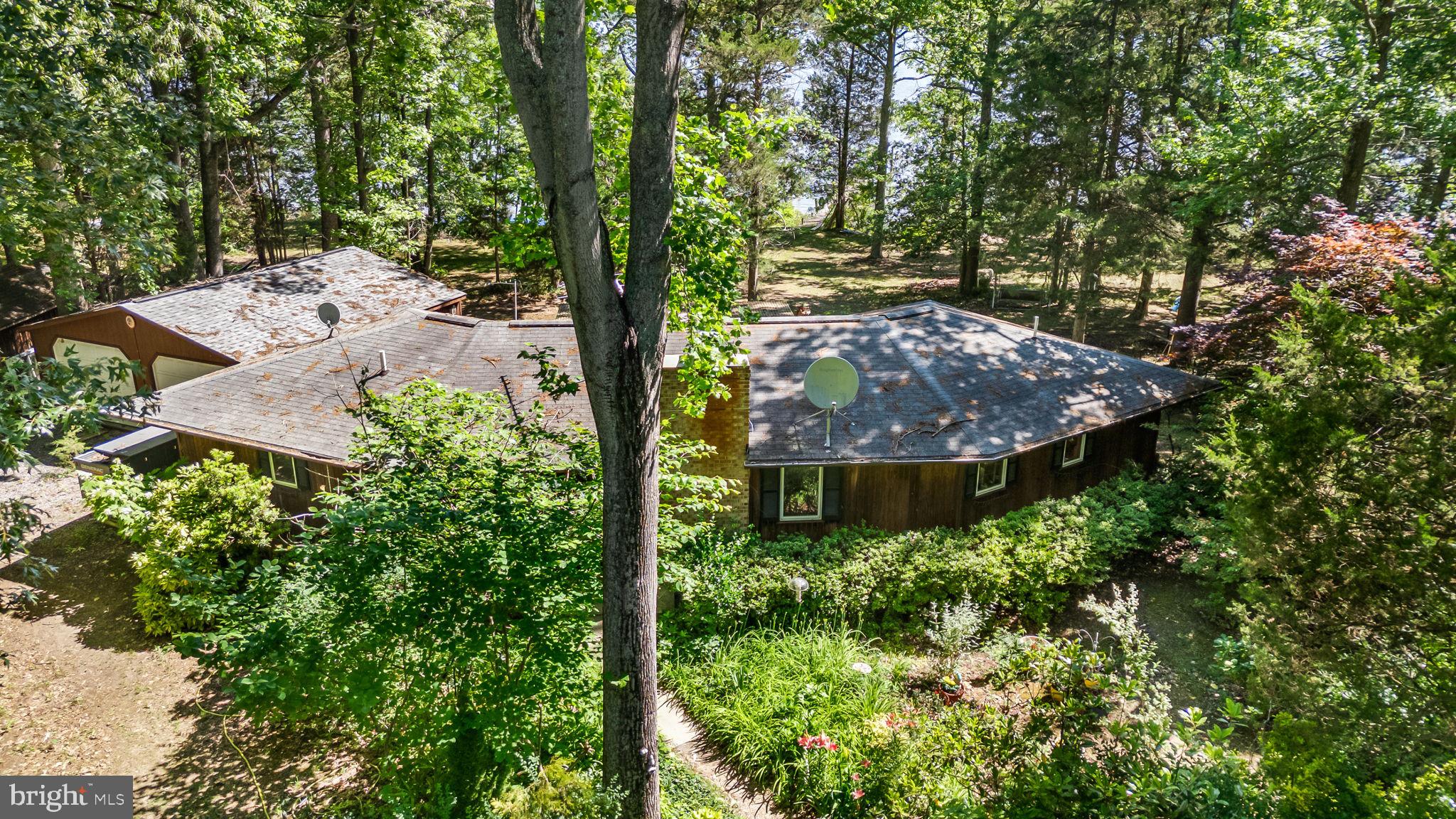 Rare waterfront retreat offering privacy, protected water access, and a truly unique octagon-style design set on a level 1.36 ACRE lot with private beach and dock. This exceptional property combines peaceful waterfront living with functional outbuildings, multiple outdoor entertaining spaces, and scenic water views from nearly every angle. Whether used as a full-time residence or weekend getaway, this home offers a lifestyle that is increasingly difficult to find. The centerpiece of the home is the dramatic open-concept great room featuring cathedral ceilings, parquet flooring, track lighting, ceiling fan, and a striking brick fireplace with wood stove insert replaced approximately two years ago. The spacious living area is designed to maximize natural light and water views while creating a warm and inviting atmosphere for relaxing or entertaining. The renovated kitchen, updated in 2015, opens seamlessly to the great room and features updated cabinetry, solid surface countertops, stainless steel appliances and abundant workspace. Both bedrooms are thoughtfully positioned for privacy and direct outdoor access, each featuring its own private exit to separate decks overlooking the water. The primary suite includes a private full bath and walk-in closet, while the secondary bedroom offers direct access to another full bath and generous closet space. Additional interior features include a dedicated laundry room with full-size washer and dryer, utility sink, storage space, electric water heater, recently replaced HVAC system (approximately one year old), attic access, and a whole-house Generac backup generator for added peace of mind. Outdoor living is exceptional with a screened porch overlooking the water, two open-air bedroom decks, private beach area, and approximately 60-foot private dock situated on protected water ideal for boating, fishing, kayaking, or simply enjoying the tranquil surroundings. The detached two-car garage provides additional convenience, while the separate detached cottage with covered porch and electric offers flexible space for a game room, studio, office, or guest overflow. A standout feature of the property is the expansive workshop complete with garage bay door, built-in work benches, pegboard storage, upper-level workspace with fixed stairs, lean-to storage area, and additional shed for tools and equipment. Gated access and separate driveways enhance privacy and functionality. Conveniently located within an easy drive of everyday amenities while offering the serenity of waterfront living, this one-of-a-kind property presents a rare opportunity to own a private retreat with endless recreational and lifestyle potential.