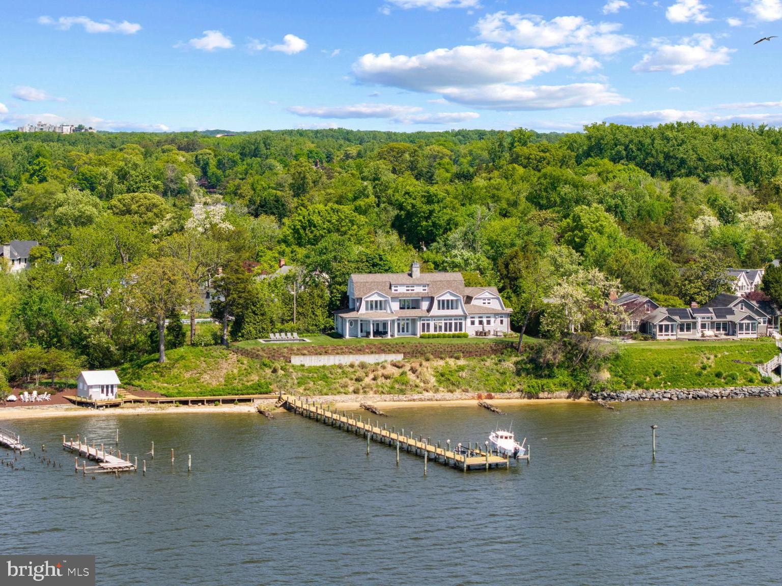 Standing proudly along the South River, just minutes from downtown Annapolis and the open waters of the Chesapeake Bay, this custom-built 2015 shingle-style residence captures the essence of refined waterfront living with a seamless balance of elegance, comfort, and connection to the outdoors. Thoughtfully designed and bathed in natural light, the home is positioned to take full advantage of its spectacular, ever-changing views, while an energy-efficient geothermal system provides exceptional year-round comfort and sustainability.

The main level is anchored by a beautifully appointed primary suite, offering a private retreat with a custom-designed closet and a spa-inspired bath. A soaking tub perfectly positioned to overlook the pool and waterfront creates a serene daily ritual, complemented by a walk-in shower and refined finishes throughout. The living spaces flow effortlessly from the kitchen to the dining area and living room, creating an inviting setting for both intimate gatherings and larger-scale entertaining, all enhanced by walls of windows that frame the surrounding landscape and water views from every room

Upstairs, two ensuite bedrooms each enjoy sweeping views of the South River, along with private balconies that invite quiet mornings and sunset reflections. The home’s thoughtful layout ensures both privacy and connection, with each space designed to highlight the remarkable setting.

Outdoors, the experience is equally compelling. The inviting waterside pool and multiple stone patios serve as the centerpiece for summer living, surrounded by impeccable, professionally curated landscaping that enhances both beauty and privacy. At the water’s edge, a charming auxiliary structure offers endless flexibility, ideal as a studio, creative retreat, or convenient storage for waterfront essentials.

With 219 feet of shoreline and just under an acre of beautifully sited land, this exceptional waterfront setting is designed for those who truly embrace life on the water. A private deep-water, multi-slip pier equipped with two boat lifts makes it effortless to head out at a moment’s notice, whether for an early morning cruise, an afternoon of fishing and watersports, or a sunset run along the South River into the open expanse of the Chesapeake Bay. From leisurely days spent boating and exploring nearby coves to hosting friends dockside or simply enjoying the ever-changing views, this property offers a seamless connection to a lifestyle defined by freedom, adventure, and the enduring appeal of waterfront living.

Set within the sought-after Wild Rose Shores community on Ferry Point, this exceptional property delivers a rare combination of newer construction, thoughtful design, and an elevated waterfront lifestyle in one of the Annapolis area’s most desirable settings. Welcome Home!