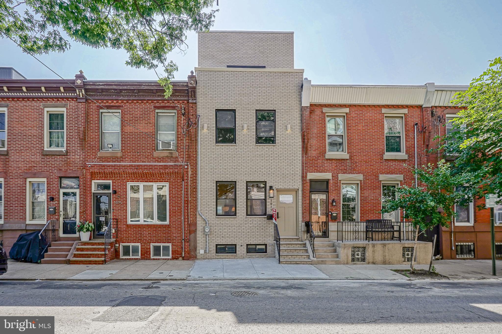 Welcome to 1917 S 3rd St, a spectacular, fully renovated 3-story contemporary townhome in the highly desirable Pennsport neighborhood of South Philly. Boasting a beautiful, classic brick front and offering just under 3,000 square feet of meticulously designed living space, this 4-bedroom, 3.5-bathroom masterpiece perfectly blends high-end luxury with functional modern living. Walk past the classic brick facade into an expansive, light-filled open-concept living room featuring premium oak luxury vinyl plank (LVP) flooring that flows seamlessly throughout the entire home.  Anchor your evenings around the custom electric fireplace in the spacious living room, which effortlessly transitions into a dedicated dining area.  A culinary dream featuring custom cabinetry with an abundance of storage, high-end stainless steel appliances, and a massive quartz island , an integrated sink, microwave, and dishwasher. Accentuated by a stunning waterfall quartz backsplash and a convenient pot filler. Perfect for hosting, the kitchen flows into an entertainer's nook featuring a massive 6-foot beverage fridge with a 111-bottle wine capacity, backed by an additional pantry, extra cabinets, and counter space. Step outside to an expansive, 30+ foot private yard—fully concreted for low maintenance and securely enclosed with crisp white vinyl fencing. The second floor hosts three bright, spacious bedrooms with ample closet space. The general bathroom features gorgeous floor-to-ceiling tile, an elegant oak vanity, and brushed gold fixtures. The front bedroom serves as a secondary junior suite, boasting its own private bathroom complete with custom two-toned tile, sliding glass shower doors, and a rich walnut vanity. The third level is a true primary sanctuary! The entire third floor is dedicated to the ultimate primary retreat. Prepare to be amazed by the master bath, showcasing a colossal 8-foot walk-in shower with floor-to-ceiling tile, dual double shower heads, and built-in niches on each side. A custom floating double vanity is set against a breathtaking sandstone accent back wall, complemented by two linen closets. Primary bedroom has 10-foot ceilings and elegant gold sconce lighting create an airy, boutique-hotel vibe. Sliding doors lead out to your private fiberglass balcony deck, offering iconic views overlooking historic Mummers Row. The walk-In closets features massive dual His & Her walk-in closets providing unparalleled wardrobe storage. Downstairs, the fully finished basement offers incredible versatility as a secondary family room, home office, or media center, complete with a convenient powder room. A separate, large mechanical room provides plenty of extra out-of-sight storage space. Situated in one of South Philly’s most sought-after communities, this home offers the ultimate neighborhood lifestyle, just steps from local coffee shops, popular neighborhood bars, eateries, and major shopping centers. Enjoy effortless access to I-95, I-76, the Philadelphia International Airport, and public transit. Located just minutes from the South Philadelphia Sporting Complex and a quick, easy ride straight into Center City. Don't miss the opportunity to own this one-of-a-kind Pennsport Gem. Schedule your private tour today!
