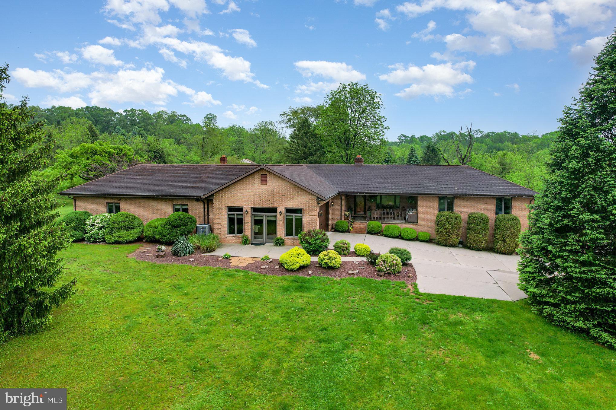 Welcome to 825 Compton Drive — a rare opportunity to own a thoughtfully designed, all-brick raised ranch nestled on nearly 14 private, partially wooded acres in desirable West Hanover Township. Combining space, privacy, and flexibility, this home offers 4 bedrooms, 3 full and 2 half baths, a 3+ car garage, and over 1,200 square feet of finished above-grade lower-level living space—ideal for multi-generational living or entertaining. The lower level features a spacious ground-level suite with no-step access, complete with an entertainment/living room, wet bar and kitchenette, bedroom, home gym/bonus room, and full bath—perfect for guests or in-laws. Upstairs, the main level boasts an inviting open layout with a formal dining room featuring hardwood floors and crown molding, a vaulted knotty pine family room with fireplace, and a gourmet kitchen (open to formal dining room) with vaulted ceiling that was designed for everyday living and gatherings. Enjoy granite countertops, a center island, breakfast bar, casual dining area, walk-in pantry, and abundant cabinetry. A spacious laundry/mudroom includes a built-in pull-out ironing board and its own half bath. The cozy but spacious primary suite offers a peaceful retreat with a sitting area, fireplace, walk-in closet, built-in bookcase, and elegant crown molding. Two additional generously sized bedrooms—one currently used as an office—and a splendid main bath complete the "west" wing of the house! Outdoor living is equally impressive: relax or entertain on the expansive paver patio with pergola, dry bar or the enclosed gazebo with hot tub, skylight, and ceiling fan, or unwind on the charming front porch. Extensive hardscaping, exterior lighting, and a detached garage/workshop with dual garage doors (front & back) enhance the property’s appeal. You’ll also find acres of private wooded trails—perfect for enjoying nature, wildlife, and tranquility just minutes from local conveniences. Looking for a family “enclave?”  Property can be subdivided, a 5 acre parcel has been engineered/approved.  A truly exceptional property and a joy to own!