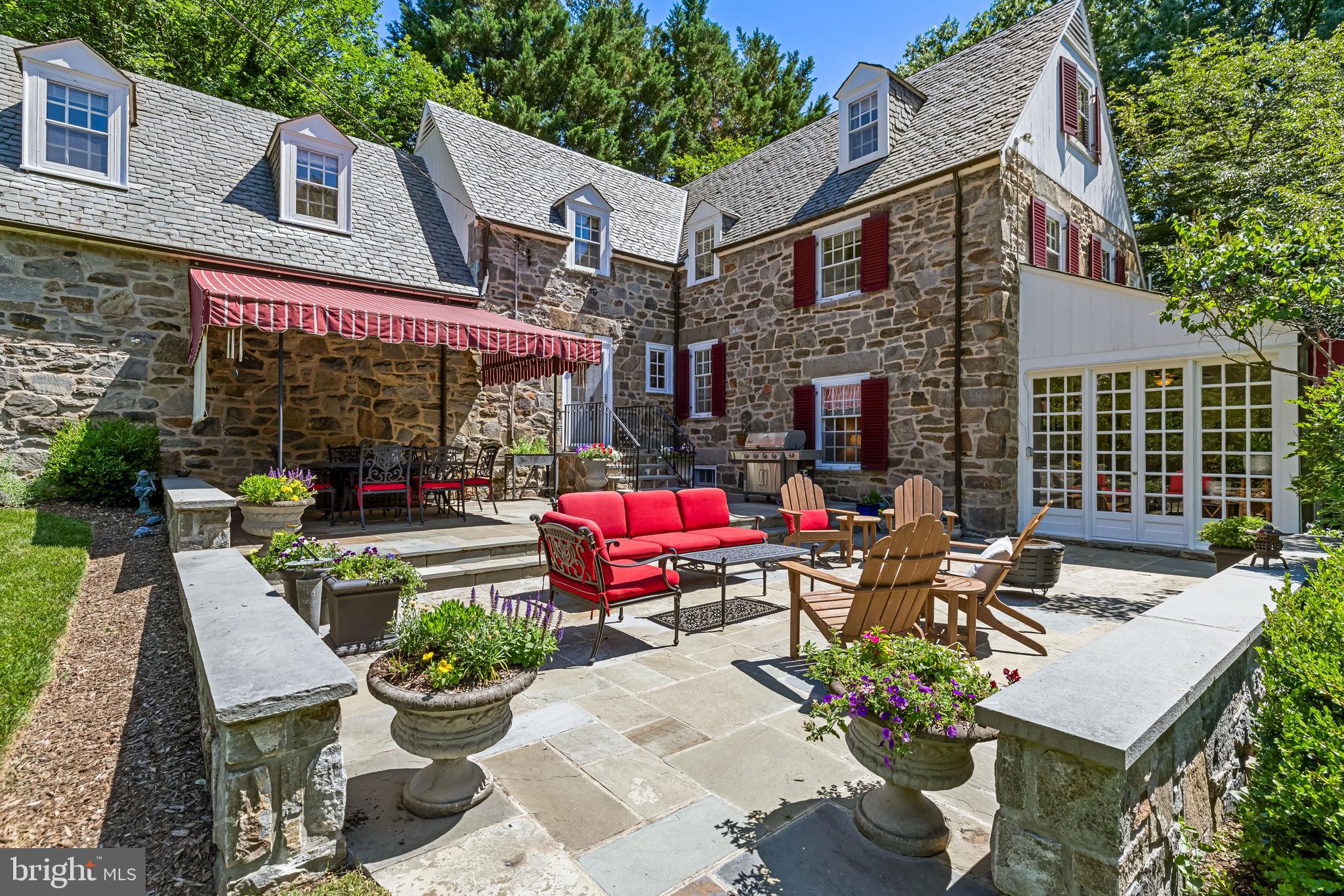 Designed by the renowned architectural firm of Palmer & Lambdin, this attractive stone residence occupies a beautifully landscaped double corner lot in the heart of Homeland, offering exceptional space and timeless architectural character.   People in the neighborhood refer to this property as “The Forsythia House” because of the colorful blooms in the spring.  The thoughtfully designed interior features a unique multi-level floor plan that creates both visual interest and functional living spaces.  The upper levels offer four bedrooms, three full baths, and a private office, providing flexibility for today’s lifestyle needs.  The main living areas include a remodeled kitchen with an island, custom cabinetry that was designed and built by Amish craftsmen, a fiveburner Thermador cooktop, double ovens and plenty of additional storage and prep space.  In addition, there is a spacious dining room ideal for entertaining as well as an impressive 24 foot living room highlighted by a wood-burning fireplace.  A bright sunroom with a wet bar and adjacent powder room extends the living space and provides the perfect setting for gatherings.  The lower level features a comfortable clubroom, an additional half bath, and a dedicated laundry room.   Outdoor entertaining is effortless on the two-tiered stone patio, complete with two awnings and overlooking a picturesque, park-like landscape.   With energy efficiency increasingly important, the seller thoughtfully enhanced the home’s existing hot water radiator system by creating eight separate heating zones, allowing for greater comfort and control throughout the residence.  Additional amenities include an attached one-car garage with interior access and a highly desirable location within walking distance of several area schools and the six decorative Homeland lakes.   A rare opportunity to own an architecturally significant Homeland home that seamlessly blends historic character, thoughtful updates, and exceptional outdoor living.  Please contact the listing agent for information regarding the National Architectural Trust Residential Conservation Easement associated with this property.