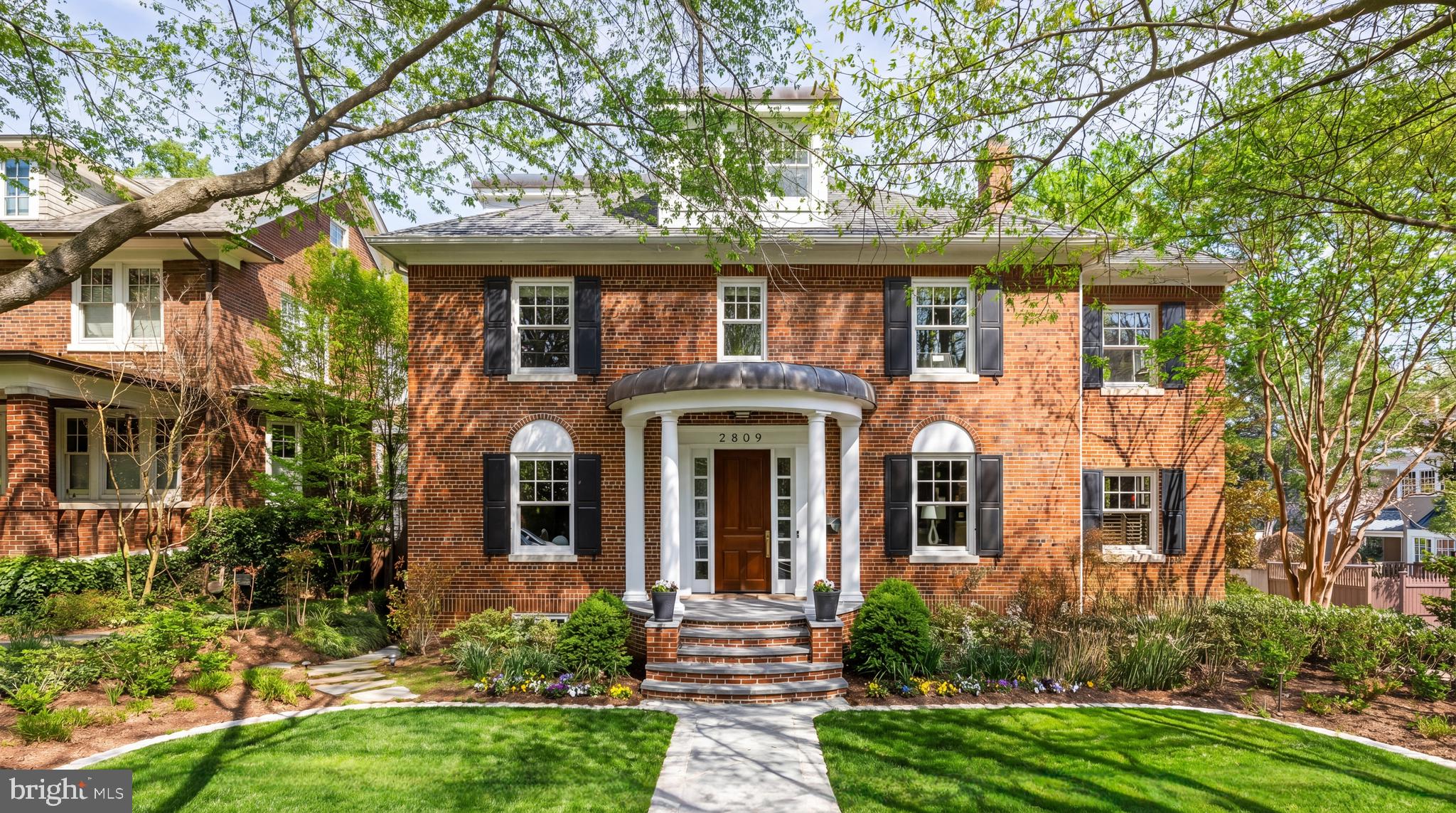 Set along a quiet, tree-lined street, 2809 34th Place NW is a residence defined by scale, privacy, and a composed architectural presence. Elevated above the street and introduced by a columned portico, the home opens to a light-filled foyer and central staircase, establishing a calm and refined sense of arrival.

The main level unfolds with quiet intention, where formal rooms and everyday living spaces coexist with fluidity. The living room, centered on a fireplace, is filled with natural light throughout the day and is equally suited for quiet mornings or evenings in company. The dining room continues this sense of proportion, accommodating larger gatherings while remaining inviting for more intimate occasions. A wood-paneled study with built-in shelving offers a private retreat, set just apart from the home’s primary flow.

Thoughtfully positioned between the dining room and kitchen, a sizable butler’s pantry introduces an added layer of functionality and discretion. Outfitted with a second dishwasher, sink, wine refrigerator, and generous counter space and cabinetry, it functions as a dedicated preparation and staging area, supporting seamless entertaining while preserving the kitchen’s sense of composition and ease.

Toward the rear, the home transitions into a more relaxed setting. The family room, anchored by a fireplace and oriented toward the surrounding grounds, becomes a natural place to gather. Just beyond, the kitchen is both functional and considered, centered around a substantial island that encourages daily life to unfold with ease. Paneled double refrigerators, double wall ovens, and a Viking gas range are seamlessly integrated, while the adjacent breakfast area offers a quieter place to begin the day.

From here, the connection outdoors is effortless. A deck extends from the main level, overlooking the pool and stone terrace below. Afternoons give way to evening, whether spent by the water, dining al fresco, or simply stepping away for a moment of quiet. Enveloped by greenery, the setting offers a sense of complete privacy.

Upstairs, the home continues with a graceful sense of separation and flow. The primary suite is set apart and accessed via its own staircase off the family room, creating a true retreat. Centered around a gas fireplace, the bedroom incorporates a sitting area and wet bar designed for daily living. The bath is finished with dual vanities, a soaking tub, and a walk-in shower, complemented by multiple dressing areas with custom built-ins. Additional bedrooms are thoughtfully positioned, each generous in scale and served by well-appointed baths. The top level features a vaulted ceiling suite with its own full bath, ideal for guests or extended stays.

The lower level mirrors the home’s scale and continuity. A large recreation room anchors the space, accompanied by a secondary sitting area and a dedicated gym or wellness room. A guest bedroom and full bath are tucked away, with ample storage throughout. A detached two-car garage is positioned at the rear of the property.

2809 34th Place NW unfolds gradually, each space building upon the last. Defined as much by feeling as by function, it offers a rare balance of comfort, elegance, and quiet sophistication.