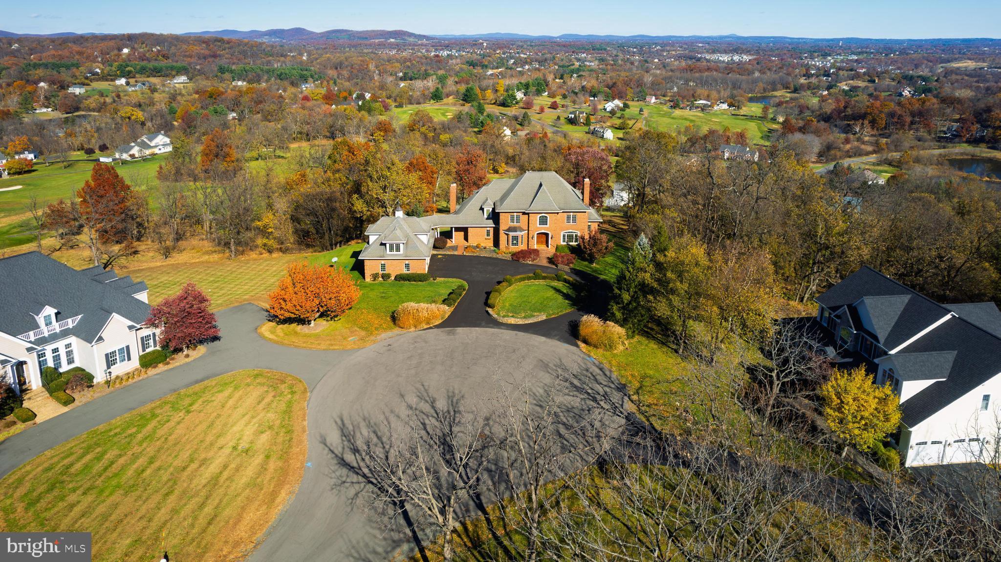 Experience resort-style living within Stoneleigh Country Club community in this French Provincial style, all-brick custom estate, perfectly positioned on one of the most beautiful lots in the area. Set on nearly 3 private acres 🌳 at the end of a quiet cul-de-sac, this exquisite well-built home welcomes you with a grand horseshoe driveway accented by vintage stone walls and mature landscaping. Blending timeless elegance with comfortable livability, this home offers 4,920 square feet throughout two levels, with breathtaking mountain and golf course views ⛰️⛳, a 3-car garage with an unfinished loft, a cupola with weathervane, a covered breezeway, and abundant storage throughout. Well-designed for both grand entertaining and multi-generational living, the residence features 5 bedrooms, 4 full baths, and 2 half baths, and includes two primary suites—one on the main level and one on the upper level.

Upon entry, a dramatic circular mahogany staircase and rich mahogany hardwood floors set a tone of warmth and sophistication. The formal dining room showcases a tray ceiling, bay window, and a well-appointed butler’s pantry with a barrel ceiling, cabinetry, wine rack, sink, and pocket doors. An inviting living room with fireplace provides flexible use, while the expansive great room impresses with a floor-to-ceiling stone fireplace, custom built-in bookshelves, and a wall of windows framing panoramic views of the Catoctin, Blue Ridge, and Sugarloaf mountains. Pocket doors allow for optional separation between the great room and the gourmet kitchen, which features cherry cabinetry with pull-out shelving, granite countertops, a center island, and a spacious eat-in area overlooking the picturesque setting. A secondary staircase provides convenient access to the upper level. Just off the kitchen, a Trex deck ☕🍷 offers the perfect spot for coffee at sunrise or wine at sunset. Another room adjoining the kitchen features a vaulted mahogany ceiling and gas fireplace, creating a cozy atmosphere. Also on the main level is a large laundry/mudroom with cabinetry and sink, two conveniently placed half baths—plus additional closets and built-in storage.

The main-level primary suite features mountain views, a walk-in closet, and a spa-inspired bath with double sinks, a soaking tub, and a walk-in shower. Upstairs, the luxurious primary suite offers a relaxing sitting area with a tray ceiling, a three-sided fireplace and built-in media cabinet, a large walk-in closet with wet bar, and access to another Trex deck 🌅. The en suite bath has dual sinks, a jetted soaking tub, and walk-in shower. Three additional bedrooms are located on the upper level—one with a private bath and two sharing a hall bath.

The unfinished walk-out lower level, with 10-foot ceilings, multiple windows, two bathroom rough-ins and exceptional storage capacity, provides an outstanding opportunity for future finished space. The unfinished loft above the garage also offers flexibility for additional storage, a workshop, or studio.

Outdoor living is a defining feature of this peaceful setting, with mature landscaping providing year-round color and privacy. It is perfectly suited for dining, entertaining, or simply enjoying the tranquil surroundings. Located within the Stoneleigh Country Club community ⛳, residents have access to a scenic championship golf course, clubhouse, tennis courts, and a swimming pool—all set amidst the natural beauty of western Loudoun County’s rolling countryside. This impressive location offers exceptional convenience—just 30 minutes to Dulles International Airport ✈️, approximately an hour to Washington, D.C., and nearby access to Route 7, local wineries 🍷, dining, and shopping. With low HOA dues of $75 per year and the benefit of public utilities (no well or septic), this one-of-a-kind estate offers the perfect blend of luxury, privacy, convenience, and lifestyle. Schedule your private tour today.