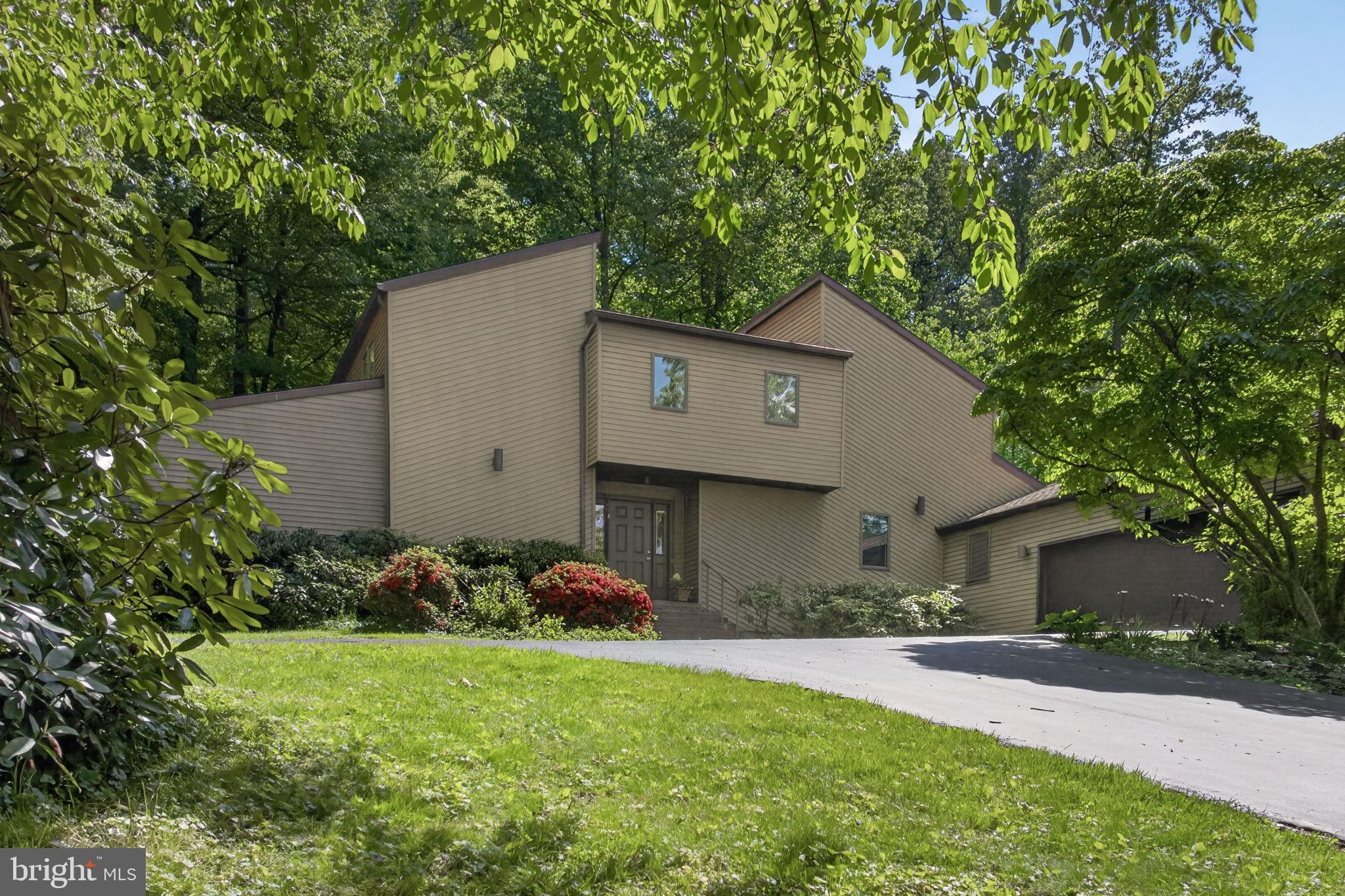 Set on a private, wooded .91-acre lot, this contemporary two-story home offers 2,850 square feet above grade, plus about 900 finished square feet in the lower level. The home includes 3 bedrooms, 2 full baths, and 2 half baths, with a layout that provides a variety of living and gathering spaces. The vaulted primary suite features a fireplace, an en suite bathroom and a screened balcony overlooking the trees. The main level includes a first-floor office with built-ins, a sunken living area, and a double-sided fireplace shared between the living and dining rooms. A hot tub room addition offers potential as a sunroom, first-floor bedroom, or additional living space. The kitchen features Corian countertops and connects to the main living areas, including a charming breakfast room with a large circular window. Expansive decks provide great outdoor living space, and the setting offers privacy while still being in an incredibly convenient location.