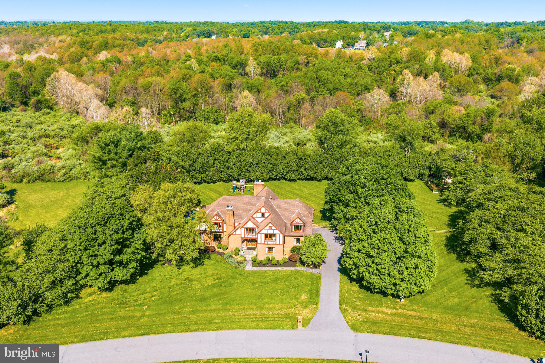 Tucked within prestigious Bridle Crossing in North Potomac, this custom Tudor estate rests on 2+ scenic acres surrounded by mature landscaping, open green space, and equestrian trails, offering exceptional privacy and timeless estate charm. Step inside the dramatic two-story foyer, where soaring ceilings, elegant millwork, oversized windows, and rich wood flooring create an immediate sense of space and sophistication. Designed for both grand entertaining and comfortable everyday living, the home features a breathtaking two-story family room with a floor-to-ceiling stone fireplace, walls of windows, built-in beverage station with dual wine refrigerators, custom chandelier, and sun-filled morning room with direct deck access. The beautifully renovated kitchen (2023) showcases upgraded cabinetry, new countertops, premium Bosch appliances, center island, and seamless flow into the breakfast area and family room. A main-level bedroom suite with adjacent full bath and separate private office offers exceptional flexibility. Upstairs, the expansive primary suite serves as a peaceful private retreat featuring soaring ceilings, hardwood flooring, gas fireplace, sitting area, oversized windows overlooking the picturesque grounds, and two walk-in closets. The spacious en suite bath is filled with natural light from multiple skylights and includes dual vanities, soaking tub, and separate shower. The upper level also features three additional spacious bedrooms, 3 full baths, walk-in closets, and a convenient laundry room, all connected by dramatic open-to-below hallways that enhance the home’s airy architectural design and natural light. The fully finished walk-out lower level expands the home’s living and entertaining possibilities with an enormous recreation room, dedicated media room, exercise room with sauna, full bath, guest bedroom, and multiple flexible-use spaces .  The outdoor setting is truly spectacular: Expansive deck overlooking the in-ground pool, sprawling open grounds, and serene wooded backdrop, an ideal setting for entertaining, recreation, gardening, quiet relaxation, or simply enjoying the ever-changing beauty of nature: Spring brings spectacular blooming ornamental trees reminiscent of cherry blossoms, summers are filled with lush greenery and glowing sunset views, autumn showcases vibrant foliage, and winter transforms the property into a peaceful snow-covered sanctuary.
Beyond its beauty, the home has benefited from substantial recent infrastructure investments rarely seen in resale properties. An extensive whole-house plumbing project exceeding $35K was recently completed with full WSSC permitting and inspections under current construction codes, including replacement of all polybutylene plumbing, updated systems to new energy-efficiency requirements, hot-water recirculation,  and modern temperature safety features. Additional upgrades include a new well pressure tank, new 75-gallon water heater, upstairs Carrier gas HVAC system (2022), whole-house well water treatment and softening system (2023) and Hayward Pro Series pool filtration system (2023), providing exceptional long-term value and peace of mind. Additional highlights include 3 fireplace, hardwood flooring throughout all three levels, feshly painted interior, spacious three-car garage. Located in the highly sought-after Wootton High School cluster, this exceptional residence offers peaceful estate living with remarkable convenience to Kentlands, Downtown Crown, Rio, Potomac Village, shopping, dining, scenic Potomac Bridle & Hiking Trails, North Potomac Community Recreation Center, Big Pines Local Park, and easy access to I-270 and I-495.