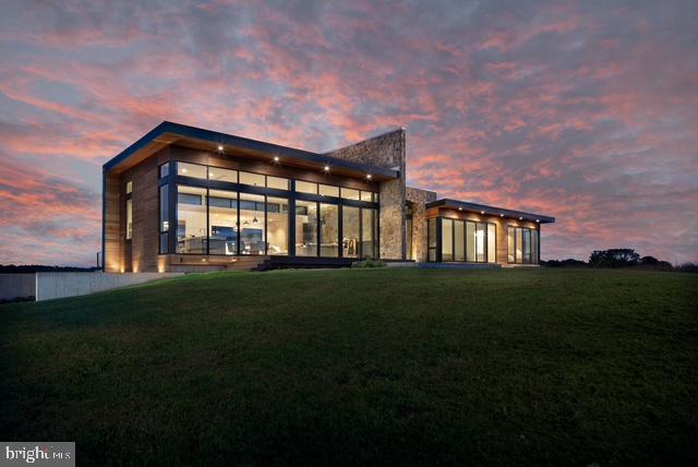 Amidst rolling hayfields and sweeping mountain views, House of Sky is a modern retreat designed for serenity and connection to nature. The striking stone-and-wood exterior opens to expansive western windows framing the Blue Ridge horizon. Designed by Lavinia Pasquina Fici and John Nahra, the home blends artistry with function in an exceptional 53-acre setting with hayfields, vineyard, and orchard.

Inside, the open kitchen/dining/living space soars with 15’ ceilings, bleached white oak floors, and walls of glass. Custom Cabico cabinetry, Brazilian granite, Caesarstone, and top appliances—Wolf, Sub-Zero, Bosch, and Grohe—make the kitchen a chef’s dream. Sliding doors lead to terraces for outdoor dining and entertaining.

The primary suite features floor-to-ceiling windows, a luxurious travertine bath with soaking tub, radiant heat, and spacious closet. A second bedroom with built-in bunks, private library, and lower-level wine cellar complete the home. Additional highlights include a garage, well-equipped laundry, and radiant floors.

Located just 5 minutes from Washington, VA, and 10 minutes from Sperryville, this extraordinary property offers modern design, peaceful solitude, and proximity to fine dining, boutique shops, and the best of Rappahannock living.