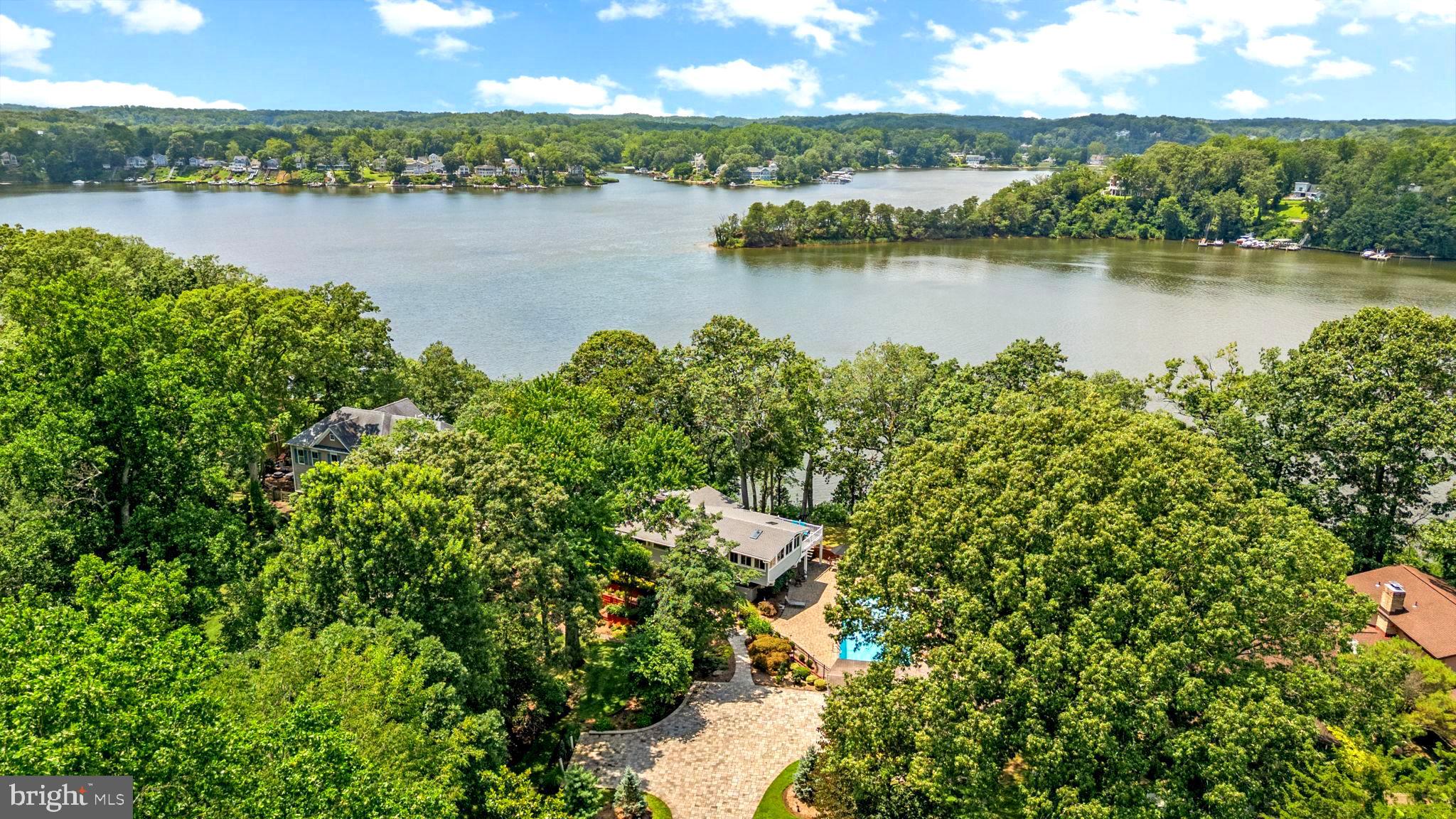 Welcome to your South River waterfront dream home! This stunning contemporary offers over 3,000 square feet of beautifully designed living space, featuring 3 bedrooms, 2.5 bathrooms, hardwood floors, neutral tones, and high-end finishes throughout. Greeted by an abundance of natural light and sweeping river views, the open-concept living area features an electric fireplace and flows seamlessly into a versatile sitting or dining area. The kitchen boasts ample cabinet and counter space, natural gas appliances, counter seating, and a built-in wine fridge—perfect for entertaining. Just off the kitchen, the all-season sunroom overlooks the pool and back deck and includes its own heating and cooling system, making it a cozy retreat year-round. The spacious primary suite is a serene escape, complete with heated floors, wall-to-wall windows with deck access, and breathtaking river views. The luxurious en-suite bath offers a tiled glass shower, soaking tub, generous walk-in closet, and a smart vanity mirror with built-in TV. The walkout lower level provides a large recreation space with a gas brick fireplace, heated floors, two additional well-sized bedrooms, a full bath, and a convenient laundry area.
Step outside to enjoy the expansive deck—ideal for watching boats glide by or hosting sunset dinners. The lower patio features a large saltwater pool, surrounded by beautifully lit landscaping, creating the ultimate outdoor oasis. Boating enthusiasts will love the spacious dock with water, power, two lifts, and a storage shed. Additional highlights include a detached two-car garage, attic storage above the primary bedroom, a front and rear irrigation system, and a large retaining wall. Conveniently located near shopping, dining, entertainment, and major commuter routes. Experience the best of waterfront living—schedule your private tour today and start living the ideal Annapolis lifestyle!