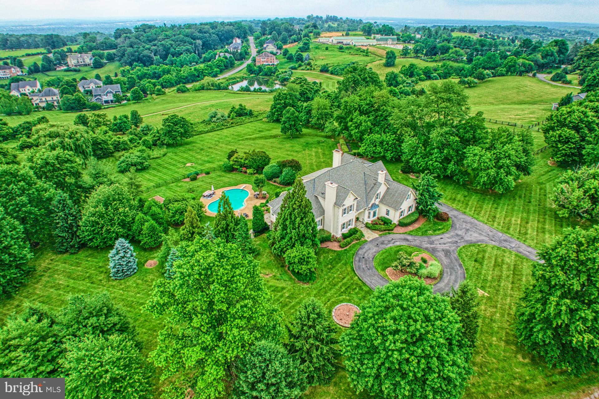 Tucked within Beacon Hills’ rolling neighborhood of custom stately homes, this beautiful residence wows from the start as modern French Country appeal enjoys 3.16 pastoral acres dotted by manicured gardens, shading trees, and an enviable circular drive. Inside, 7,334 square feet are flowing and sunny as both cozy nooks and expansive living vistas feature picture windows, eye-catching hardwoods, soaring ceilings, and stone-wrapped fireplaces. Store keepsakes within the living room’s navy-hued cabinetry with beam-inspired open shelving, tend to office-tasks among beautifully displayed collections, and let the loft host playdates and quiet conversation. In the recently renovated kitchen, plan the day at the center island, while granite countertops, high-end appliances, and endless cabinetry assist with heirloom recipes.  Set meals in the formal dining room or window-wrapped breakfast nook, and celebrate summers outside where a sprawling deck, stone patio, and pool welcome grilled bites and cannonballs. When the weather cools, your lower level entertains with bar, climate-controlled wine room, and places for exercise, creativity, and favorite films. After a day exploring nearby historic townships, five expansive bedrooms soothe. While guests may enjoy the lower-level bedroom with full bath or private attic-level retreat, your first floor primary offers a suite complete with steam shower, jetted place for bubbles, and sweeping property views. While on tour, visit the oversized laundry, and note three car garage where you’ll store vehicles, sports equipment, and tinker with weekend projects. From home, explore historic Leesburg, perfect your swing on signature golf courses, and enjoy tastings and annual festivals throughout vibrant Hunt and Wine Country.