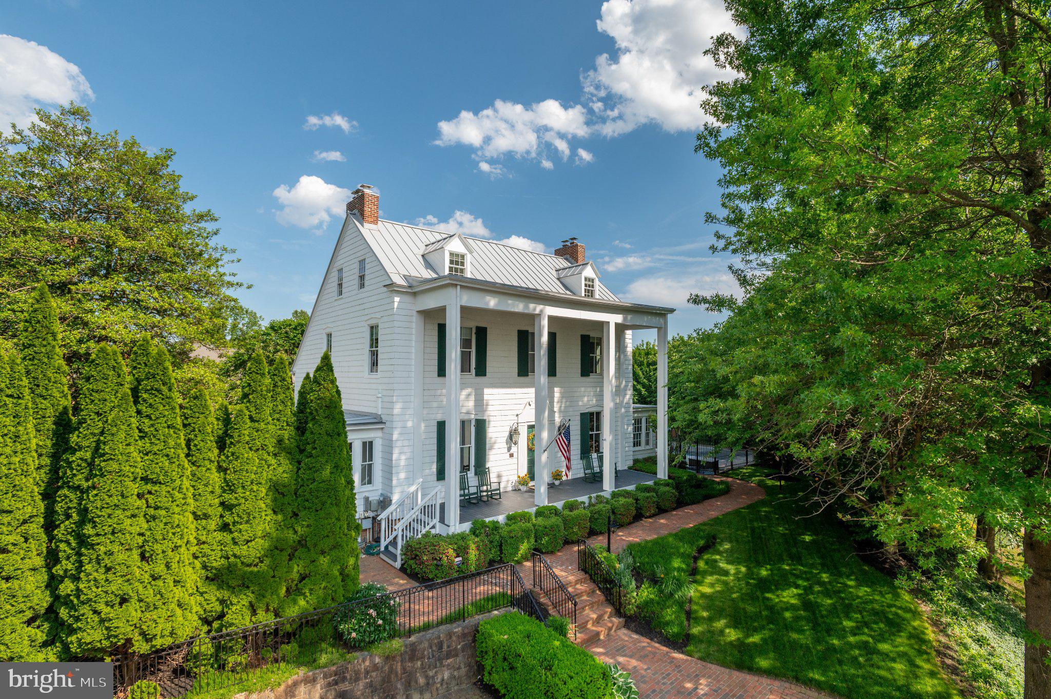 Open Saturday and Sunday 1-4 - Known as the Fuller-Schuerman House, this remarkable Fairfax City residence stands among the area's most iconic historic properties, set facing Pickett Road in the sought-after Pickett’s Reserve neighborhood. Originally constructed in the 1850s, the grand columned Colonial has been thoughtfully restored and renovated to preserve its architectural character while incorporating the modern systems and amenities expected for contemporary living. The gracious home boasts three floors, plus a full lower level.
A stately two-story columned front porch introduces an interior defined by exceptional scale and craftsmanship. The main level features soaring 11-foot ceilings, extensive moldings, hardwood floors, period hardware, and gracious formal spaces designed for both entertaining and everyday living. A grand central staircase serves as the home's architectural centerpiece, while the formal dining room and expansive living room each feature fireplaces that reflect the property's historic pedigree. Flanking the main living spaces are two versatile bonus rooms, ideal as a private library or home office and a comfortable sitting room overlooking the pool and outdoor entertaining areas. Period door hinges, vent covers and light switches add to the historic texture of the home. 
Beyond the formal rooms, the spacious renovated kitchen offers generous table space, a gas cooktop, double wall ovens, granite counter tops, and abundant room for gathering. Throughout the home, historic details have been carefully preserved while substantial updates ensure comfort and convenience, including radiator heat and two forced-air HVAC systems. Outside, extensive landscaping surrounds the property, creating a private setting highlighted by an in-ground pool with a chld-proof, motorized cover, a large hot-tub an expansive surrounding patio and mature landscaping. A recently installed metal roof, a brick-paver parking area, and numerous thoughtful improvements further enhance this exceptional residence.
The upper levels provide five bedrooms and three full baths, including a spacious primary suite with fireplace, walk-in closet, and luxurious ensuite bath featuring a soaking tub, large shower, and separate water closet. Two additional bedrooms and a hall bath occupy the second level, while the third floor offers two additional bedrooms with exposed original beams along with a full bath, providing exceptional flexibility for guests, family members, or additional workspace. The lower level extends the home's livability with a large family room featuring a fireplace and built-in cabinetry with a quartz top and LED lighting. A full bath, an expansive workroom and an adjacent private bedroom or office finish out the lower level space. Ample storage is found throughout, including a wine closet, a pantry closet at the foot of the stairs, and a utility room with deep shelving.
Rarely does a property so successfully combine architectural presence, modern comfort, and a premier Fairfax City location. The Fuller-Schuerman House offers a unique opportunity to own one of Northern Virginia's truly distinguished historic homes.
