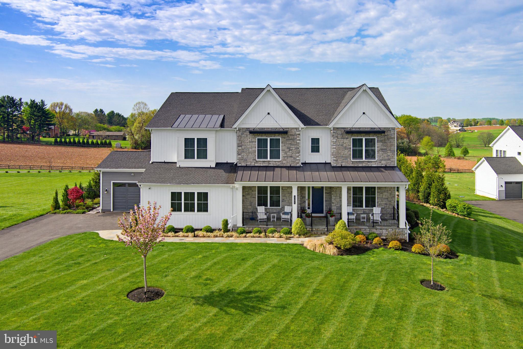 A Rare Offering! Exquisite Craftsmans style estate on 1 acre with sweeping pastoral views. This exceptional four-year-old Toll Brothers built home offers a rare combination of refined design, thoughtful functionality, and elevated indoor-outdoor living—all overlooking breathtaking pastoral scenery. A dramatic two-story great room serves as the heart of the home, highlighted by a floor-to-ceiling stone gas fireplace and expansive windows that frame the serene landscape beyond. The space flows effortlessly into a designer gourmet kitchen featuring granite countertops, an oversized center island, premium Wolf appliances, and a well-appointed prep kitchen complete with its own refrigerator, sink, dishwasher, and stove. A generous walk-in pantry adds both convenience and storage. The main level is thoughtfully designed to accommodate multigenerational living, offering a private suite with a spacious bedroom, sitting room with wet bar, luxury bath, walk-in closet, and its own dedicated laundry. Elegant details are found throughout, including custom millwork in the formal dining room and private study, along with hardwood flooring spanning throughout most of the home. Upstairs, the primary suite is a sophisticated retreat, showcasing a tray ceiling, private wet bar, and a spa-inspired bath with soaking tub, expansive walk-in shower, and ample closet space. Three additional bedrooms each feature en suite bath, complemented by a conveniently located second-floor laundry room. The fully finished lower level extends the home’s versatility with a sixth bedroom or fitness space and an upgraded wet bar with wine storage, designer tile backsplash, and custom lighting. Outdoor living is truly exceptional. A covered patio, accessed through French sliding doors from the great room, features a second fireplace—perfect for year-round enjoyment. In addition, a separate outdoor kitchen and living area includes a built-in grill, dedicated prep space, and ample room for dining with table and chairs, all perfectly positioned to take in the sweeping pastoral views. Extensive hardscaping, including a paver patio and fire pit, creates an ideal setting for both intimate gatherings and large-scale entertaining. Additional features include a whole-house generator, irrigation system for both front and rear grounds, upgraded lighting throughout, and a six-zone in-ceiling sound system. This is a rare opportunity to own a meticulously upgraded, turnkey residence offering luxury, privacy, and exceptional outdoor living in a truly scenic setting.