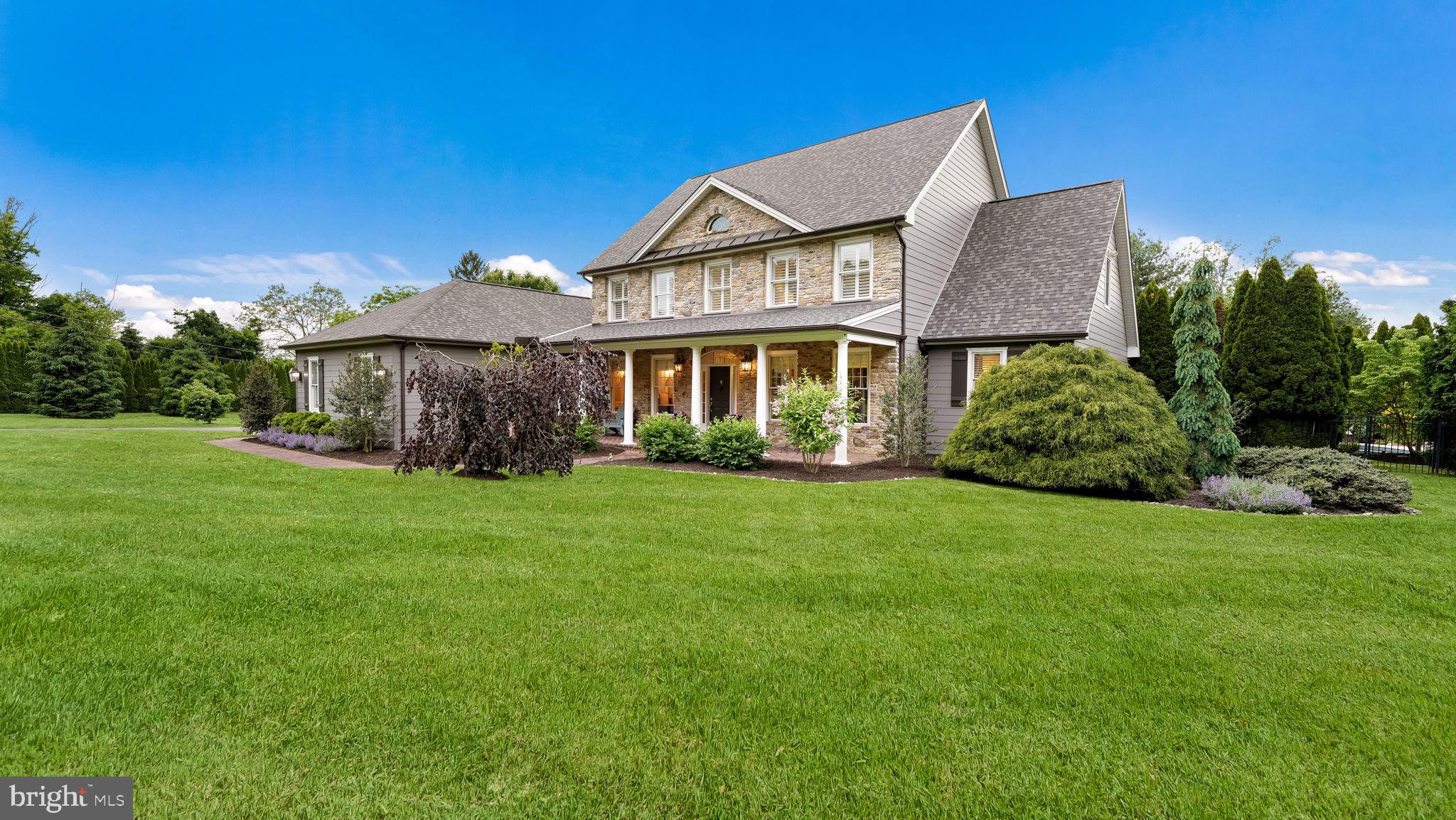 Enjoy refined Bucks County living in this exceptional Buckingham retreat, tucked within a private enclave of just three custom homes. Built by Greg Bittner and set on more than two lush, bucolic acres, this distinguished residence offers timeless craftsmanship, elegant living spaces, and a desirable first-floor primary suite.
A welcoming covered front porch sets the tone, offering the perfect place to relax with summer iced tea and take in the peaceful surroundings. Inside, a gracious center hall is flanked by formal living and dining rooms, enhanced by detailed millwork and classic wainscoting. Straight ahead, the dramatic two-story great room impresses with a soaring wall of windows and a beautiful Bucks County fieldstone gas fireplace.
The gourmet kitchen features custom cabinetry, granite countertops, an induction cooktop, wall oven, convection microwave oven, center island, and a spacious breakfast room overlooking the grounds. The first-floor primary suite enjoys serene views of the backyard oasis, an elegant tray ceiling, and French doors leading outside. The ensuite bath includes a double vanity, Jacuzzi tub, separate shower, and a walk-in closet with built-in organizers. A powder room and convenient mudroom/laundry room complete the main level.
Upstairs, you’ll find three generously sized bedrooms, a hall bath, and two versatile bonus rooms, ideal for home offices, playrooms, or additional storage. The finished lower level offers an additional 1200 sq ft of finished space for entertaining and everyday enjoyment, including a media room with Sony projector, game room, bar, exercise room, full bath, additional bonus room, and ample storage.
Outdoors, the property feels like a private resort. Enjoy a magnificent, heated pool with spa, built-in grill, custom pavilion with a stone woodburning fireplace for year-round gatherings, an oversized shed with electricity and a dryer, and a dedicated garden area for those with a green thumb.
Notable improvements during the current owners’ stewardship include the addition of Hardie Board siding around the home, a new 40 year roof, repointed brick chimney, the custom outdoor pavilion with fireplace, refinished wood flooring, and conversion of the great room fireplace to gas. The induction stove top, oven and convection oven/ microwave were just installed in May 2026. This remarkable Buckingham property offers privacy, comfort, and an elevated lifestyle in a truly special setting.