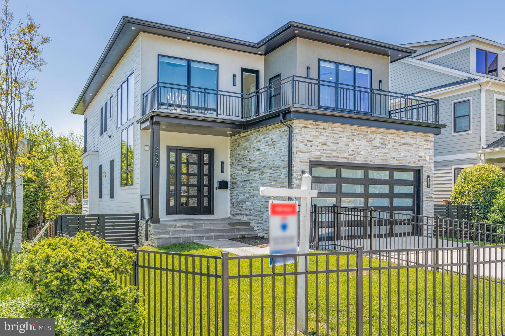 Experience contemporary luxury in this stunning, nearly new home located in the heart of Arlington’s coveted Lyon Park neighborhood. Just two years young and mere blocks from Clarendon, this modern residence offers over 4,700 square feet of refined living space, featuring six bedrooms and six-and-a-half bathrooms. Designed with striking curb appeal, it showcases a glass-paneled garage, stacked stone façade, flagstone walkway, front roof deck, and a fully fenced front yard. Inside, a grand two-story foyer with a custom chandelier and statement staircase welcomes you into a bright, open layout with 10-foot ceilings, oak floors, elegant crown molding, and custom designer window treatments throughout. The chef’s kitchen is a dream, equipped with quartz countertops, Thermador appliances, soft-close Milania cabinetry, under-cabinet lighting, a reverse osmosis filtered water system, and a large center island that flows seamlessly into the family room featuring a 42-inch gas fireplace and mounted TV.
Convenience meets style on the main level with a bedroom suite, chic powder room, and a fully functional mudroom with built-ins. Upstairs, the luxurious primary suite includes a private balcony, walk-in closet with organizers, and a spa-inspired bath complete with a freestanding tub, triple-head shower with body jets, heated Toto bidet toilet, and more. Three additional bedrooms each offer ensuite baths and ample storage, and the upper level also includes a well-appointed laundry room and access to a private rooftop deck. The lower level is a true oasis with 9-foot ceilings, a walk-out recreation room, wet bar, wine display room with French doors, a flexible gym or studio space, and a private guest suite. Enjoy outdoor living on the covered rear porch and in the spacious, fenced backyard. Additional features include a two-car garage with epoxy flooring and EV charging capability. All of this, just minutes from Clarendon Metro, Downtown D.C., The Pentagon, National Landing, and local parks and trails — a perfect blend of modern elegance and walkable urban lifestyle.